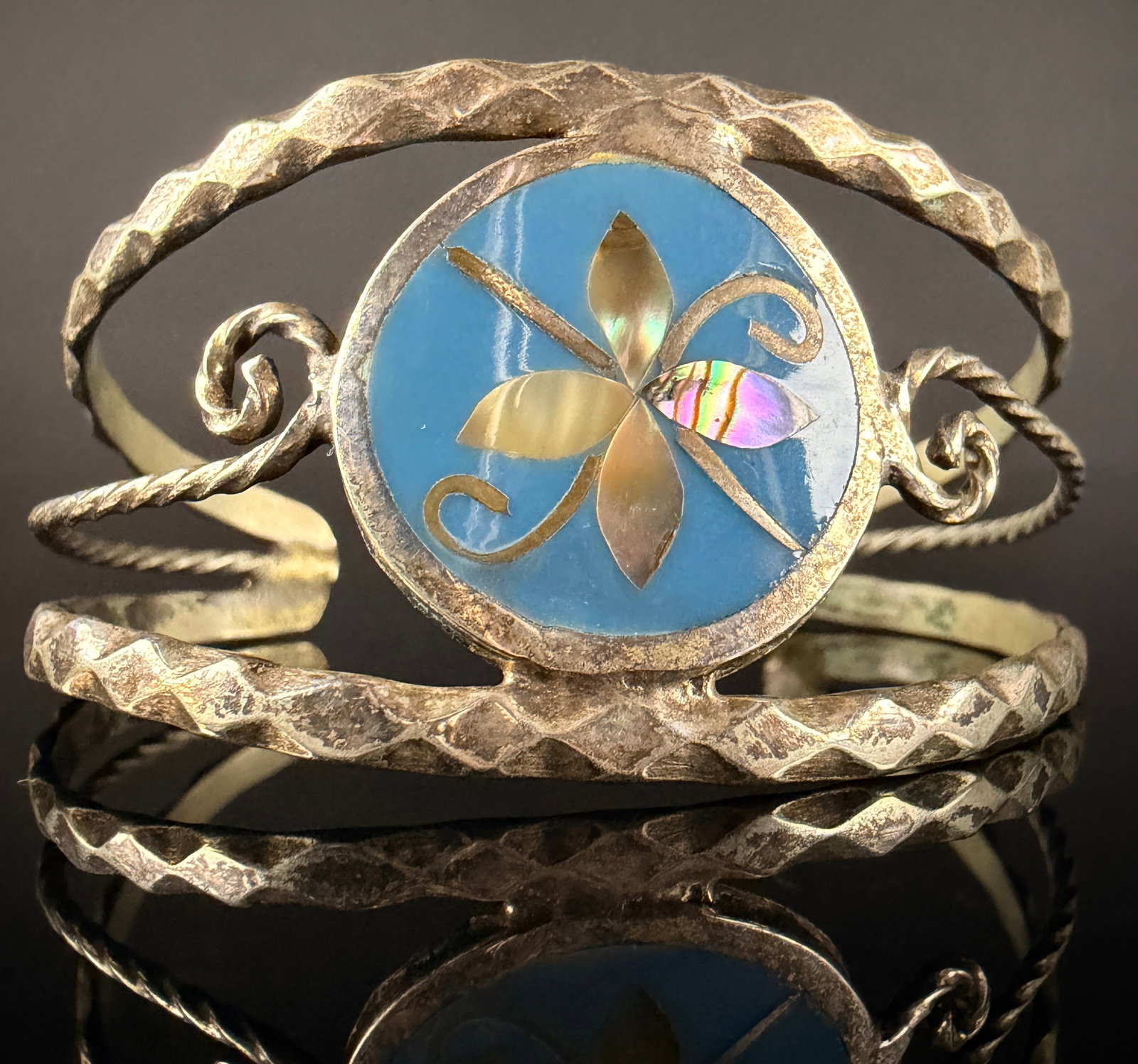Vintage Alpaca Mexico Flower Inlay Cuff Bracelet: A vintage Mexican cuff bracelet featuring a central circular medallion with a stylized floral motif. The medallion is composed of iridescent shell inlays set against a light blue ground with fine wire