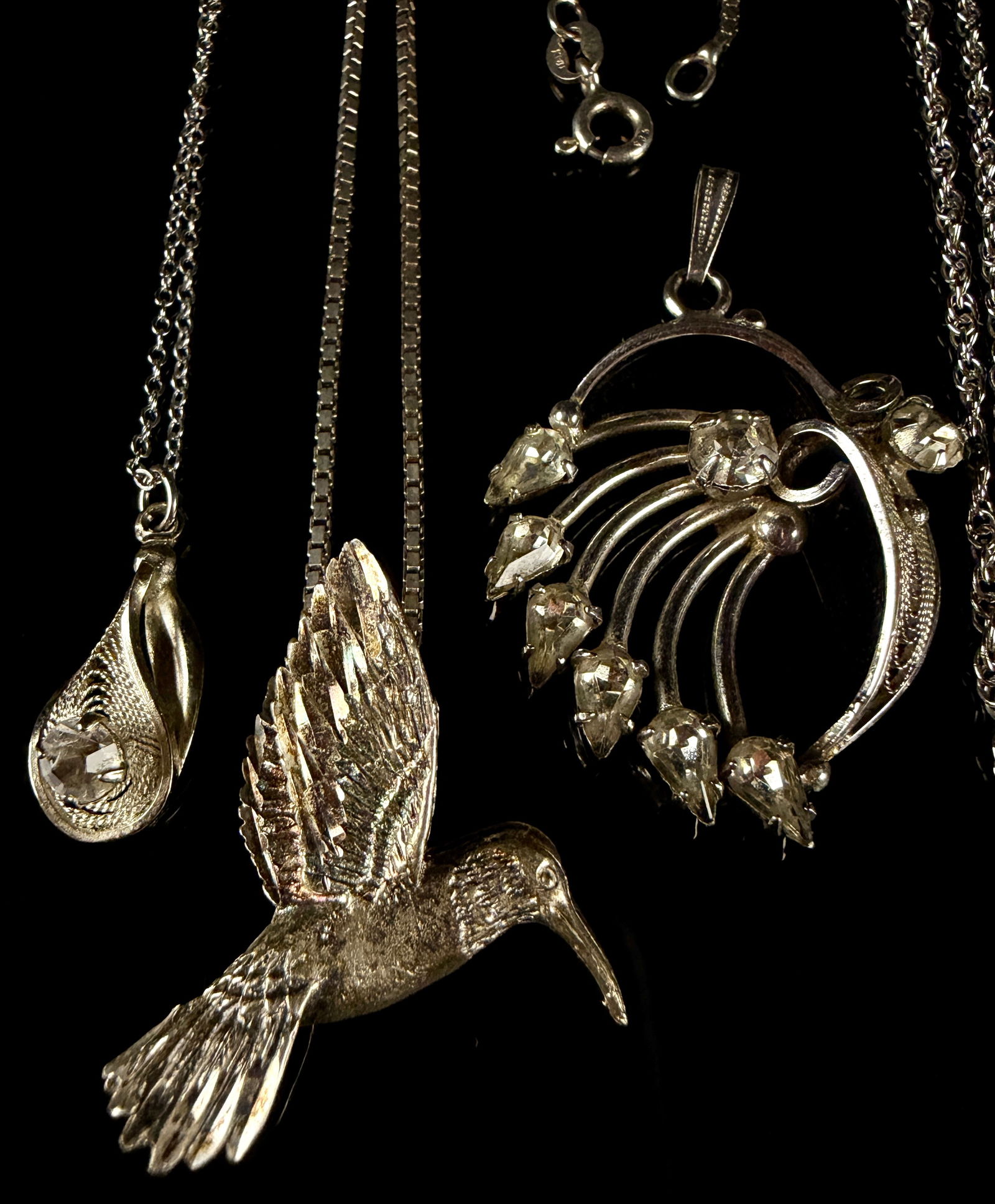 A Collection of Sterling Silver Pendants and Necklaces: An assortment of sterling silver jewelry comprising several necklaces and pendants. The group features various decorative motifs including a hummingbird, a teddy bear, an intricate filigree teardrop,