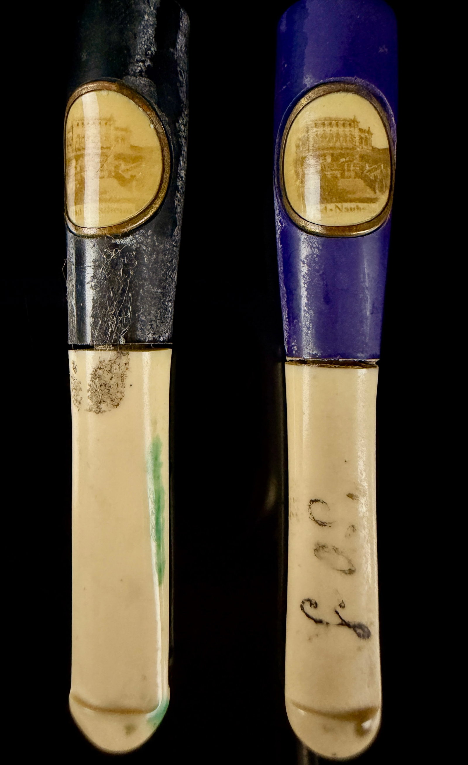 A Pair of Vintage Bad-Nauheim Souvenir Cigarette Holders: A pair of souvenir cigarette holders featuring a two-part construction. The upper sections are finished in dark tones of black and purple, while the lower sections are cream-colored. Each piece is set