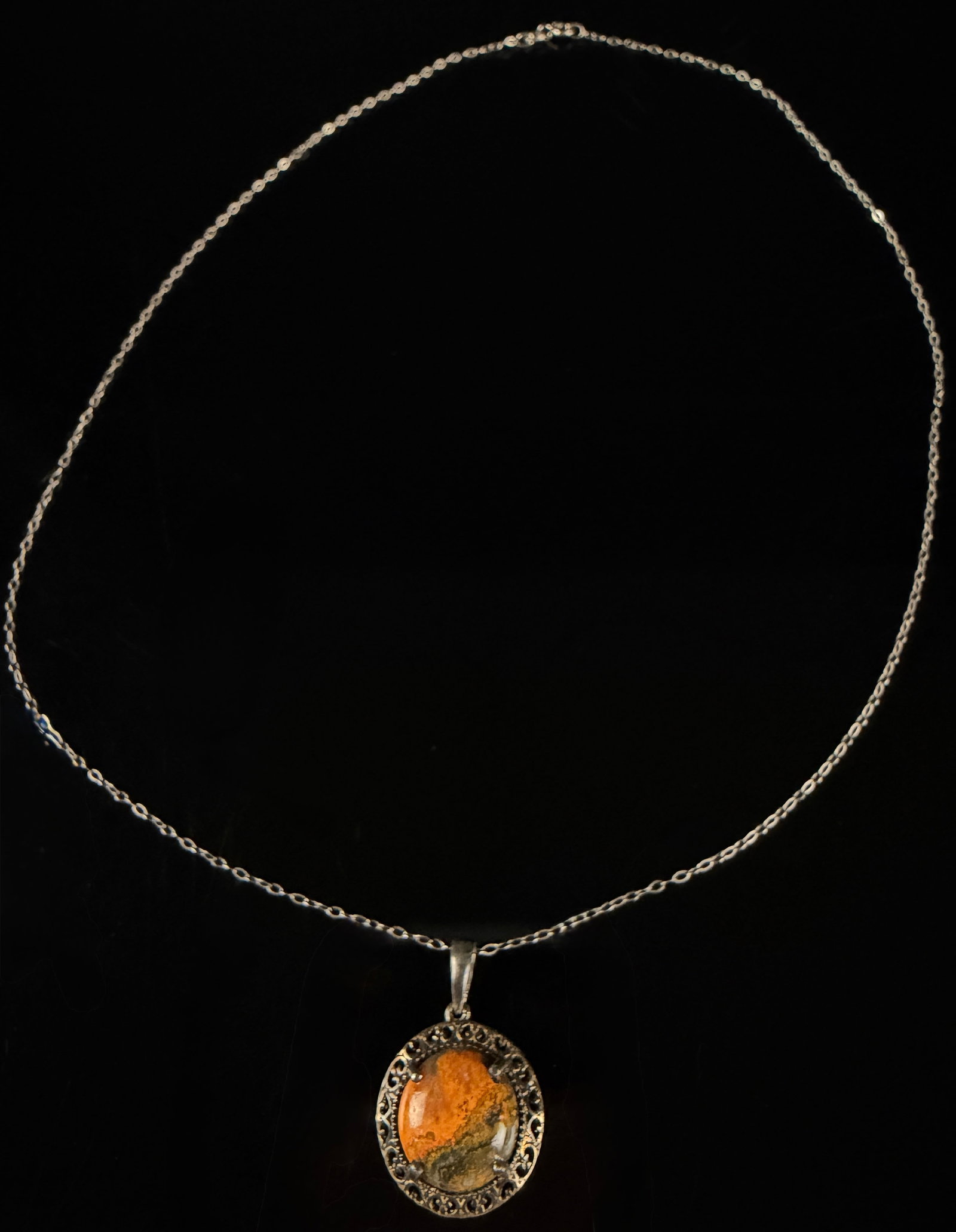 A Sterling Silver and Bumblebee Jasper Pendant Necklace: A sterling silver necklace featuring a circular pendant set with a variegated cabochon stone. The stone displays mottled orange, yellow, and dark green hues, consistent with bumblebee jasper, and is