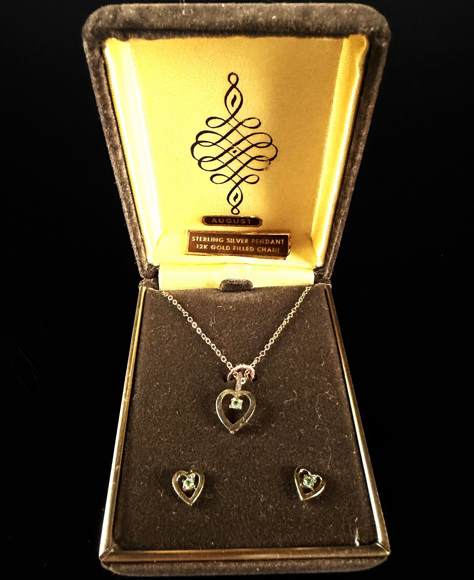 A Trio of Vintage Gold-Tone Sterling Silver and Peridot Heart Jewelry Items: A vintage jewelry set featuring an August birthstone theme, consisting of a heart-shaped pendant on a chain and a matching pair of stud earrings. The open-work heart pendant is crafted from sterling s