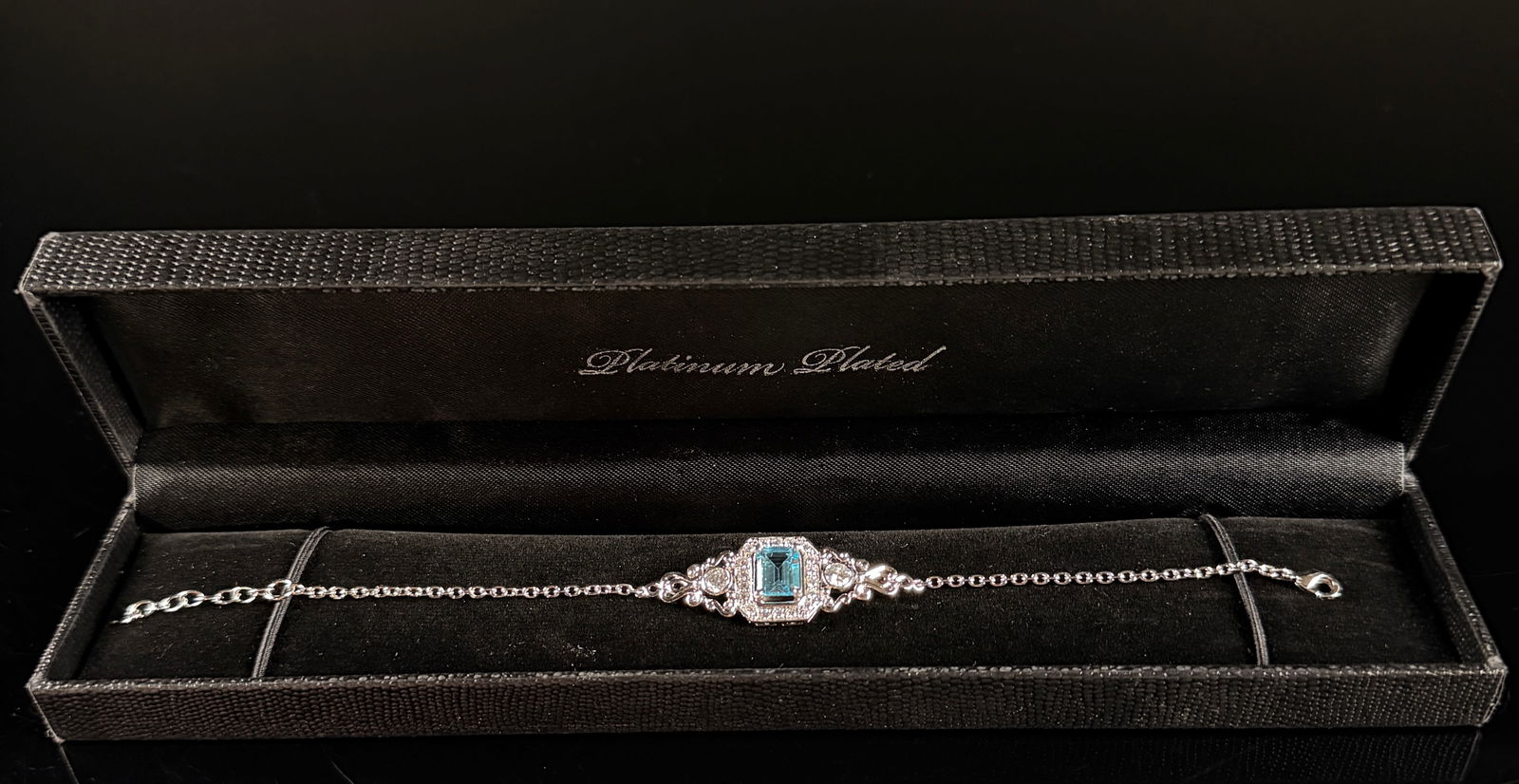 Gold Coast Platinum-Plated Art Deco Style Aquamarine Simulant Bracelet: A platinum-plated fashion bracelet by Gold Coast, featuring an Art Deco-inspired design. The centerpiece contains a rectangular emerald-cut light blue stone, likely an aquamarine simulant, surrounded