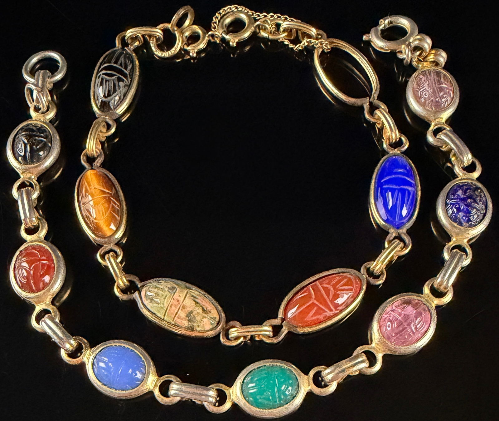 A Pair of Winard 12K Gold-Filled Egyptian Revival Scarab Bracelets: A pair of Egyptian Revival style link bracelets by Winard. Each bracelet features a series of oval-cut, bezel-set stones carved in the form of scarabs. The stones include a variety of materials and co