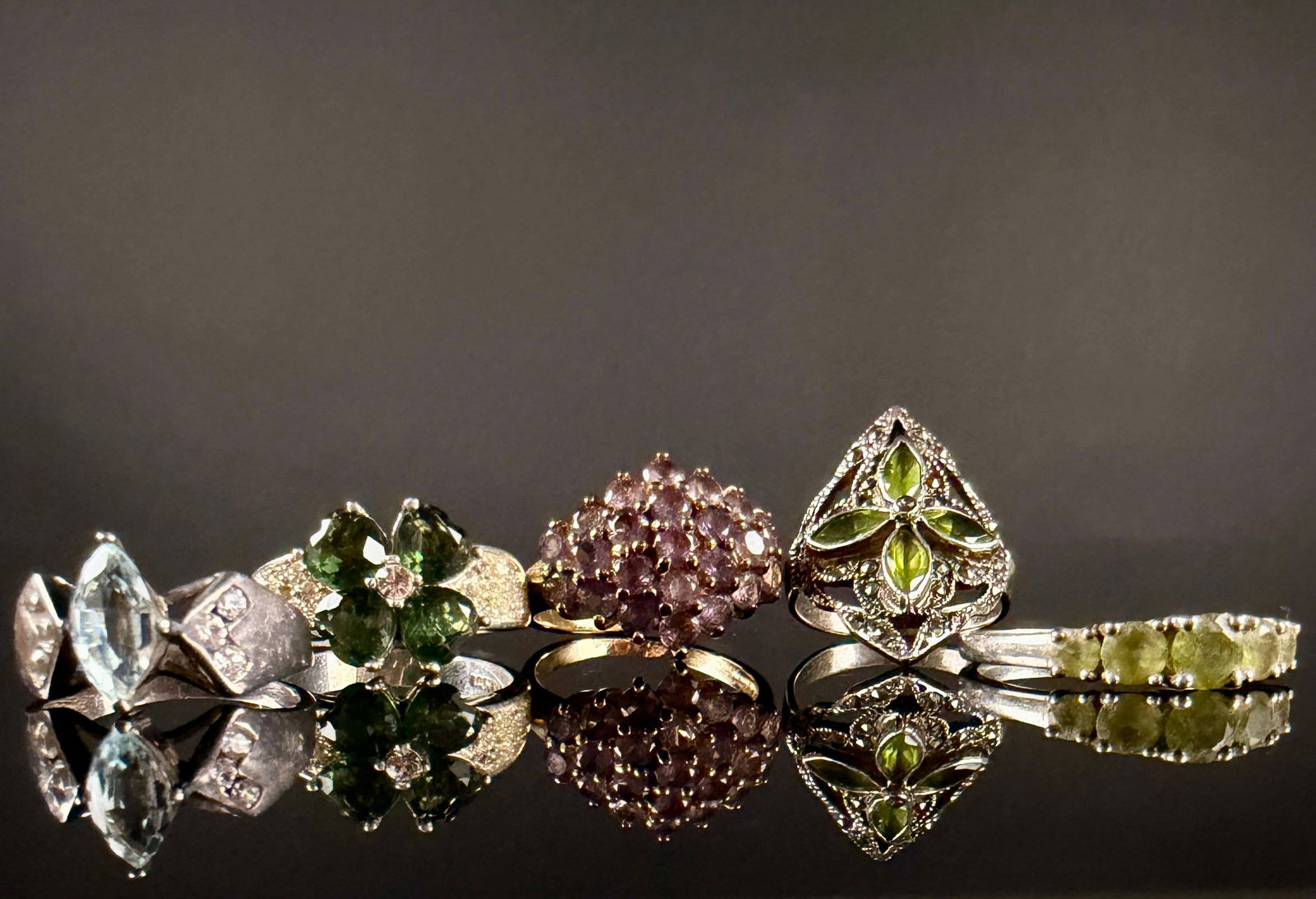 A Collection of Sterling Silver and Multi-Stone Decorative Rings: A collection of decorative rings featuring various gemstone-style settings and metal finishes. The group includes a silver-toned ring with a marquise-cut light blue stone and accent stones; a silver-t