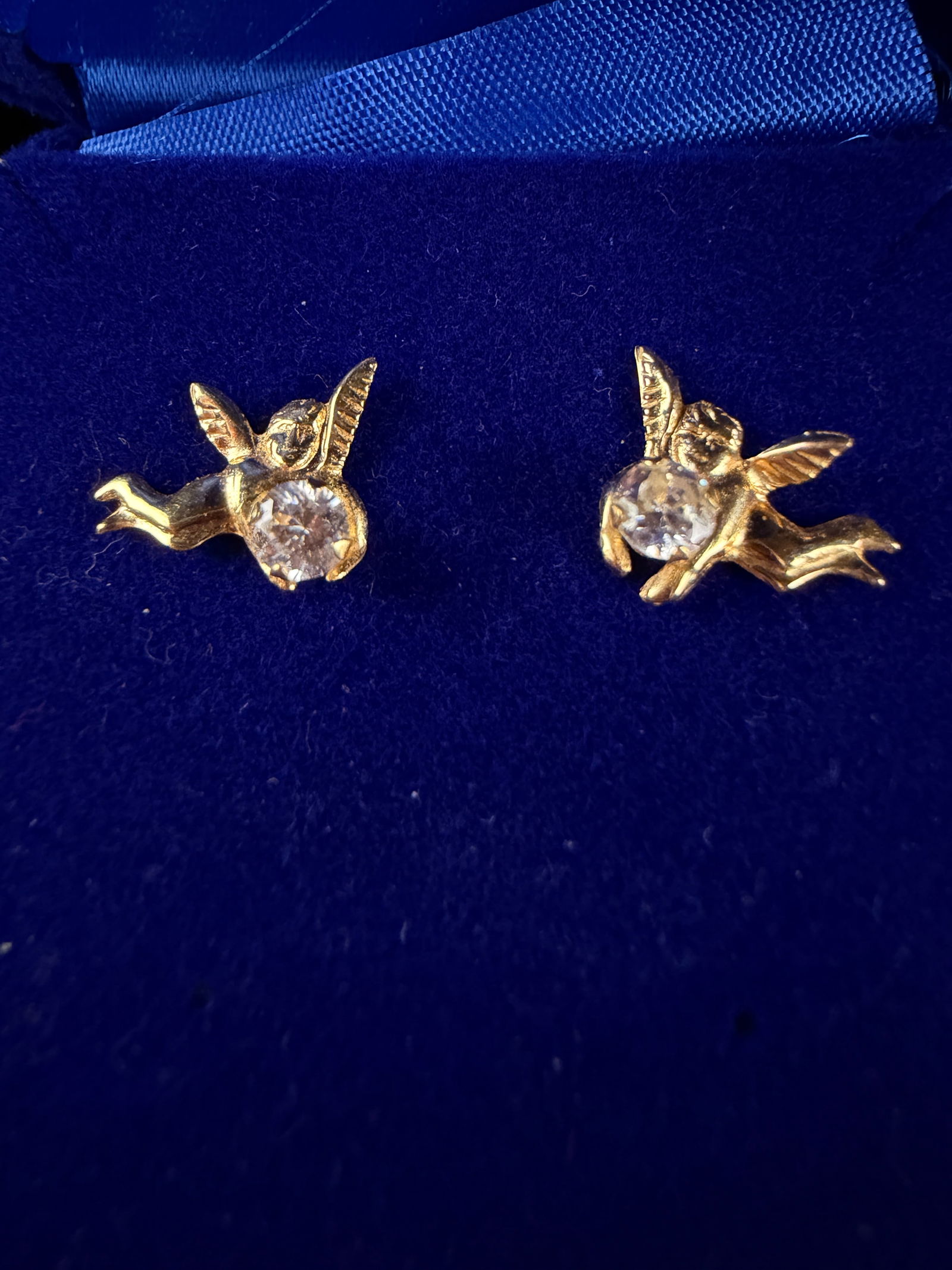 A Pair of 14K Yellow Gold and Stone-Set Cherub Stud Earrings: A pair of contemporary figural stud earrings featuring a cherub motif. Each earring is crafted in 14K yellow gold and accented by a single round, brilliant-cut clear stone. The earring posts are stamp