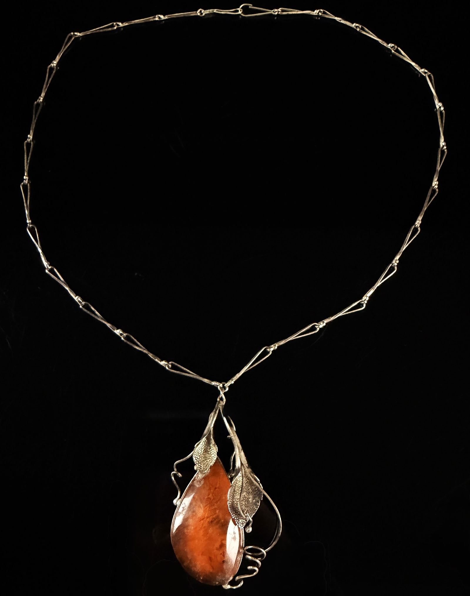 Art Nouveau Baltic Amber and 800 Silver Floral Pendant Necklace: An Art Nouveau style pendant necklace featuring a large teardrop-shaped honey Baltic amber cabochon with natural inclusions. The amber is set within a stylized 800 silver frame characterized by windin
