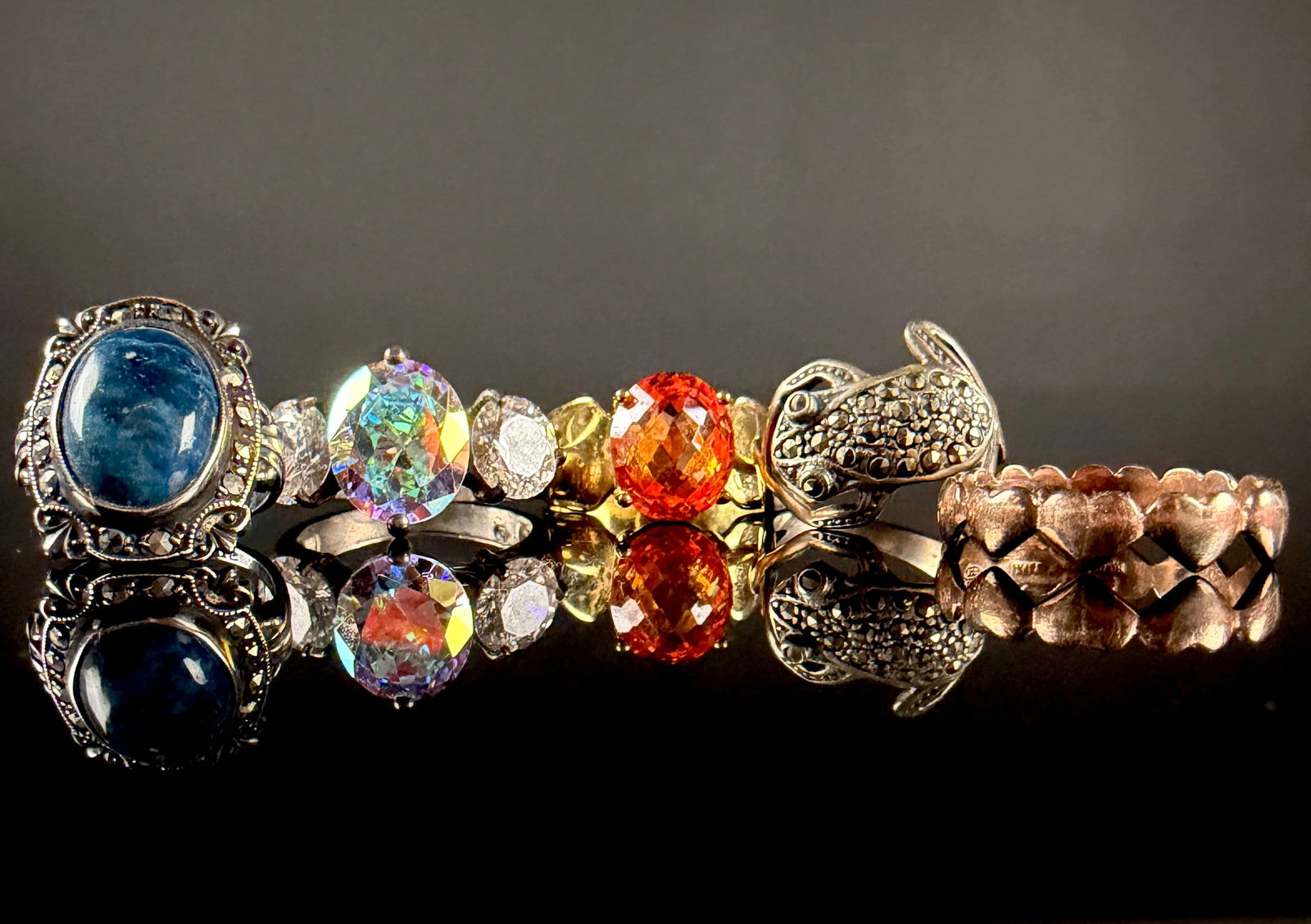 A Collection of Sterling Silver and Costume Gemstone Rings: A collection of gemstone and costume jewelry rings in various styles and materials. The group includes a sterling silver ring with a large oval blue cabochon in a decorative marcasite-set border, mark