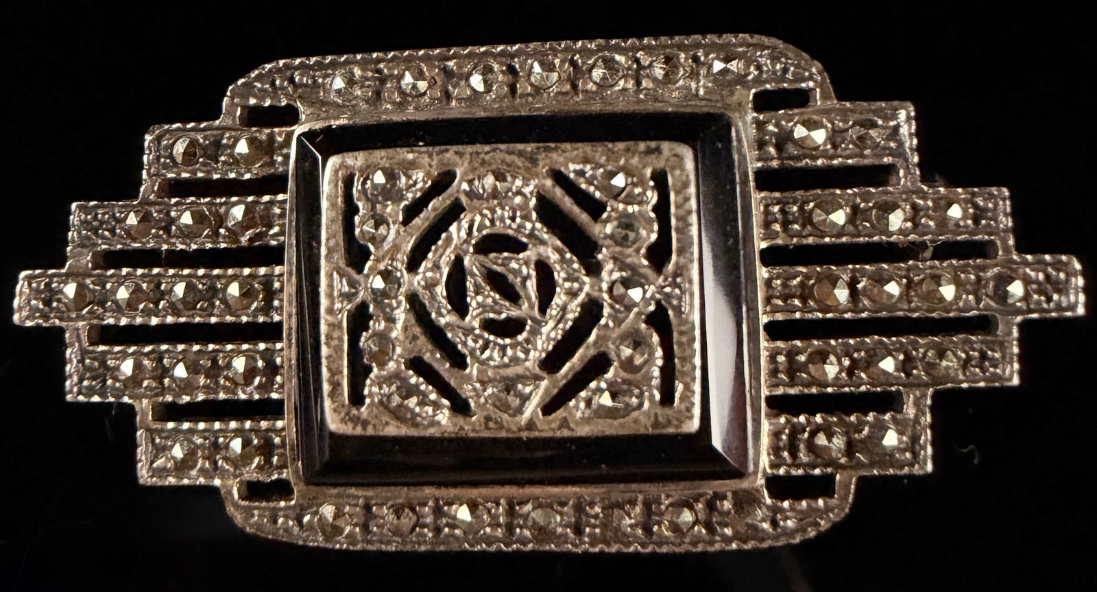 Art Deco Sterling Silver Onyx and Marcasite Brooch: An Art Deco sterling silver onyx and marcasite brooch featuring a geometric, stepped rectangular frame. The piece is set with marcasite stones surrounding a central rectangular black onyx stone. This