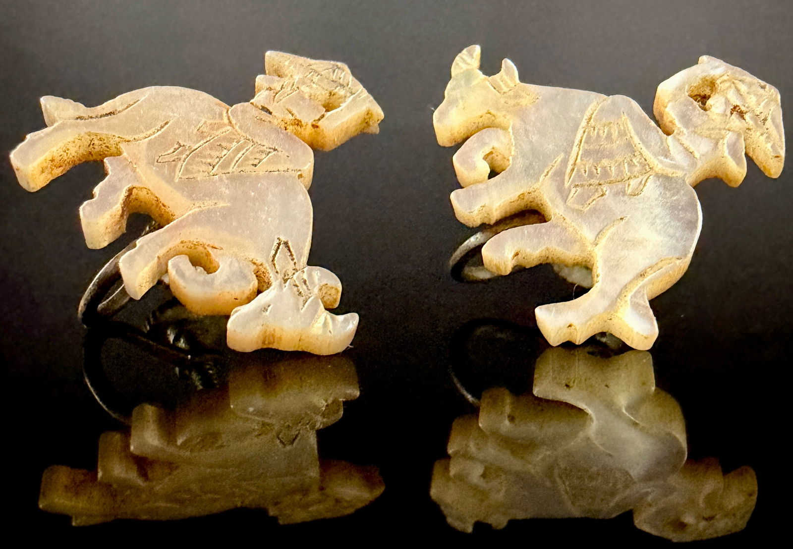 A Pair of Vintage Japanese Carved Mother-of-Pearl Cattle Dragon Earrings: A pair of vintage screw-back earrings featuring hand-carved iridescent mother-of-pearl motifs. The carved elements depict stylized figures, including a rider and a horned animal or cattle dragon, base