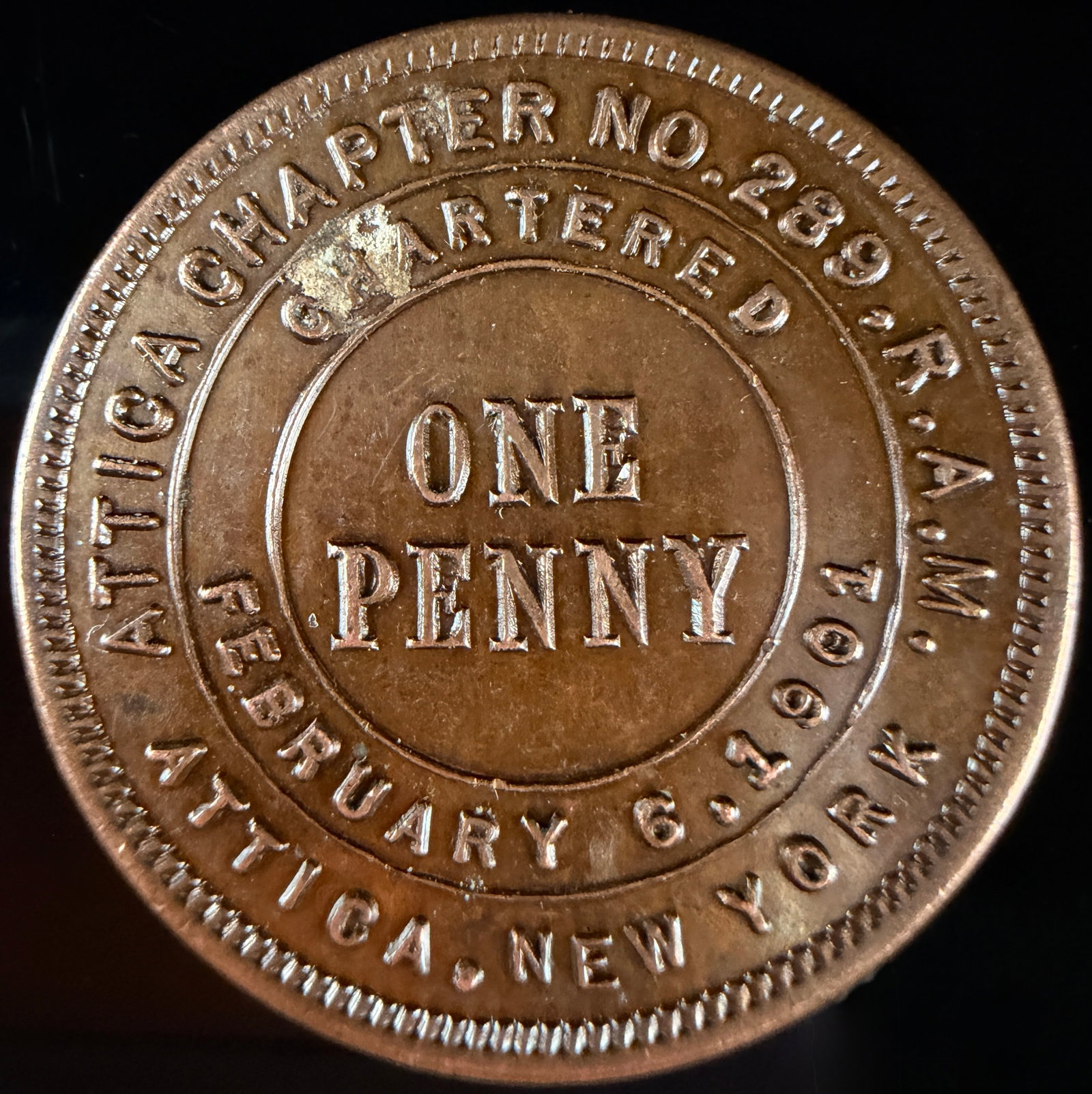 Attica Chapter No. 289 R.A.M. Masonic One Penny Token New York: A Masonic Chapter Penny token from the Royal Arch Masons (R.A.M.) Attica Chapter No. 289 in Attica, New York. Struck in a copper-colored metal, the obverse features central ONE PENNY text surrounded b