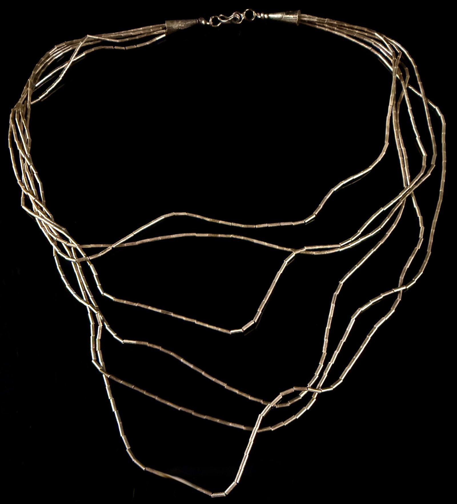 A Multi-Strand Liquid Sterling Silver Heishi Necklace: This liquid sterling silver heishi necklace features multiple strands of fine, tube-shaped beads gathered into decorative conical end caps. The piece is characteristic of Southwestern jewelry design a