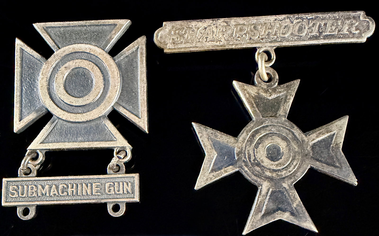 Two WWII US Army Sterling Silver Sharpshooter and Submachine Gun Marksmanship Badges: Two United States military marksmanship qualification badges from the World War II era, crafted in sterling silver. The group includes a Sharpshooter badge featuring a Maltese-style cross with a centr
