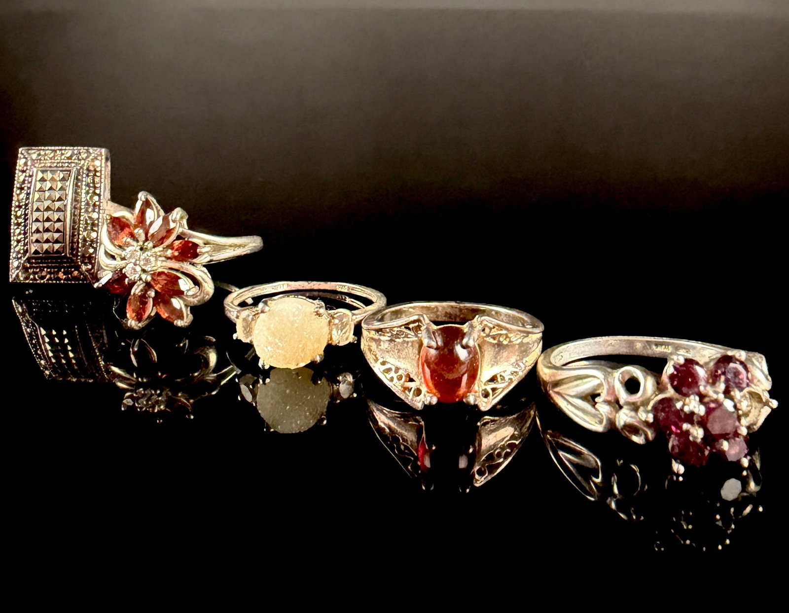 A Collection of Sterling Silver and Gemstone Rings: A collection of sterling silver rings in various vintage and contemporary styles featuring gemstone accents. The group includes two rings with floral cluster arrangements of faceted red stones, likely