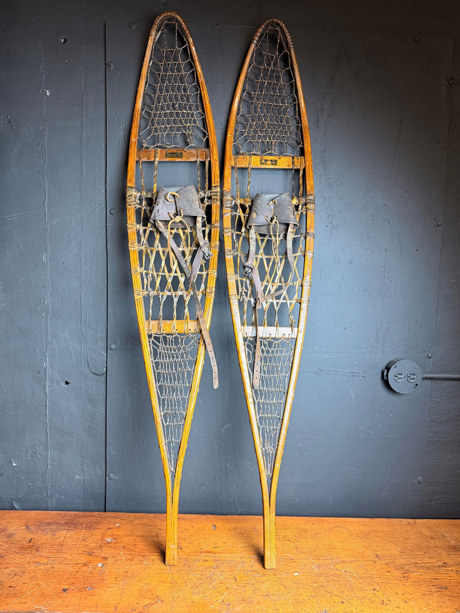 A Pair of Snocraft Inc. Wood and Rawhide Alaskan Style Snowshoes: A pair of vintage Alaskan style snowshoes manufactured by Snocraft Inc. of Norway, Maine. The frames are constructed from bent wood with a long, narrow profile and pointed tails. The interior
