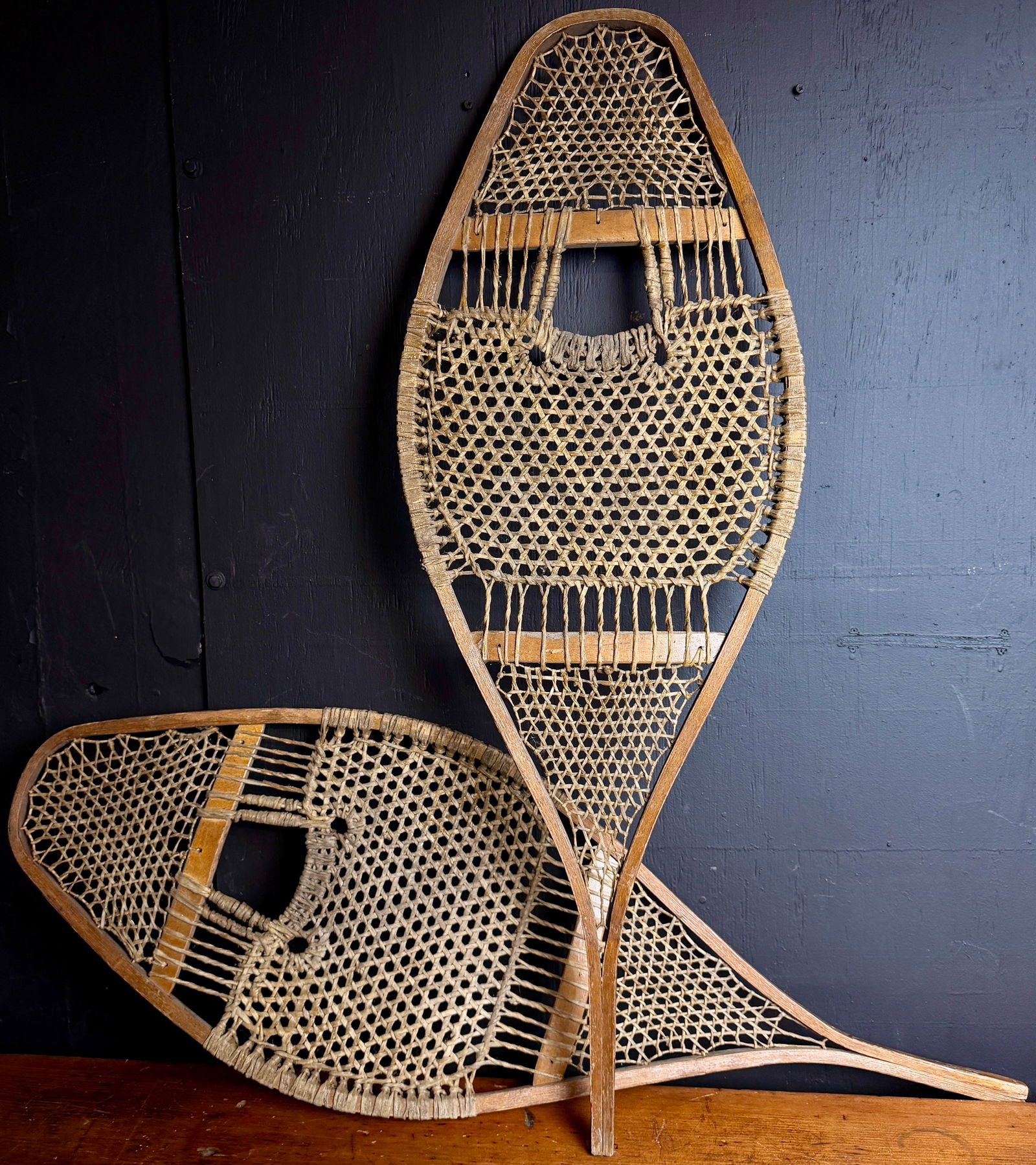 A Pair of Native American Huron Style Teardrop Snowshoes: A pair of traditional Native American Huron style snowshoes. Each item is constructed with a bentwood frame and features intricate woven rawhide or sinew lacing. The design follows a classic teardrop