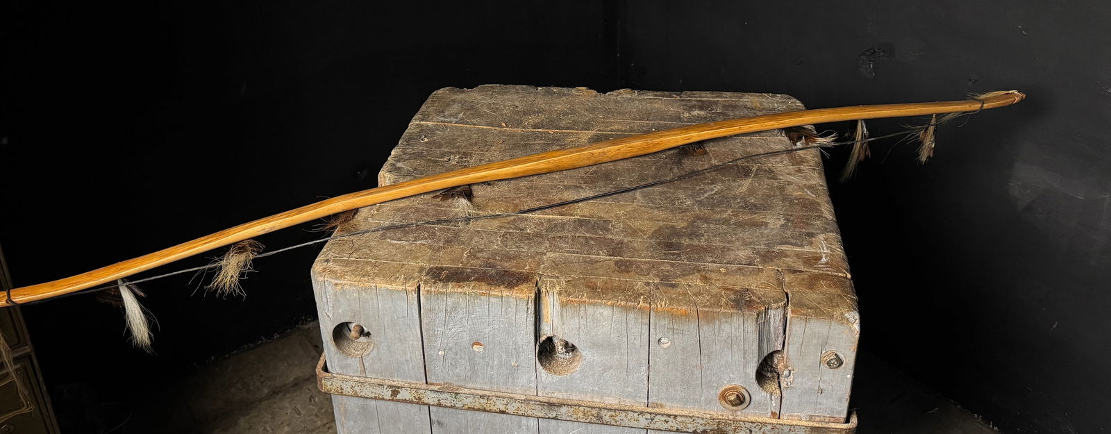 A Handcrafted Hardwood Bow with Feather and Animal Hair Decoration: A handcrafted wooden bow featuring a polished stave carved from a light-toned hardwood with a prominent longitudinal grain. The stave exhibits a reflex-deflex profile with tapered ends and simple, car