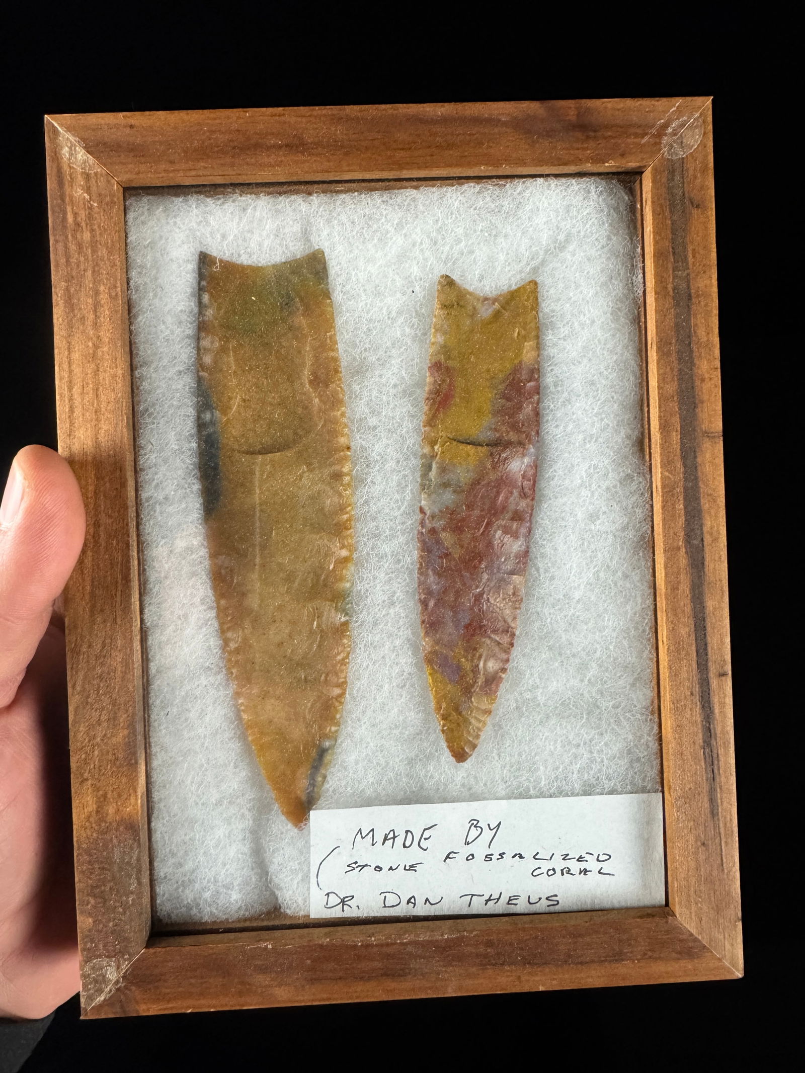 A Pair of Modern Fossilized Coral Projectile Points by Dr. Dan Theus: A pair of modern bifacial stone projectile points crafted from fossilized coral. The points exhibit a variegated color palette of ochre, tan, and mottled red-purple hues. Both specimens feature pressu