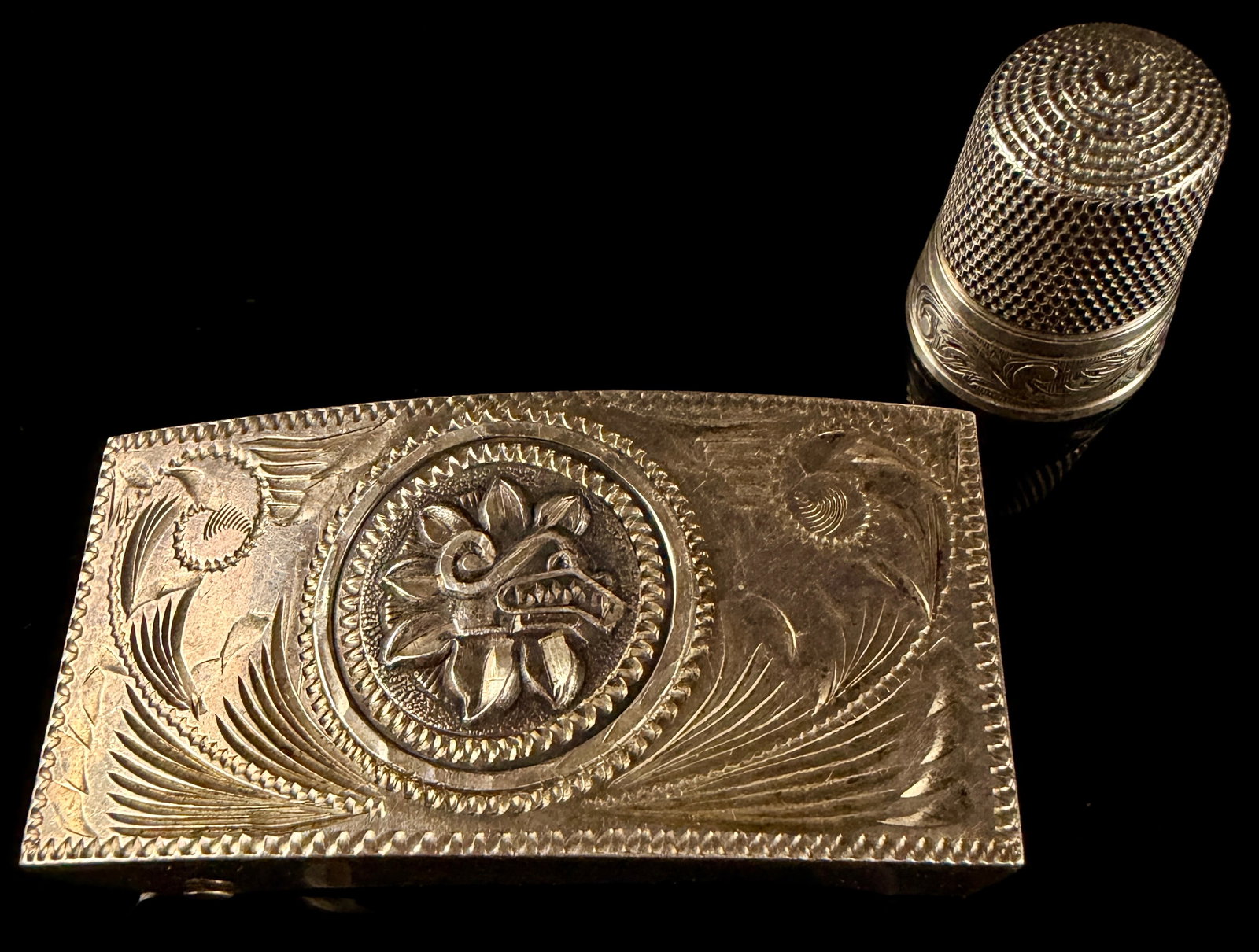 Two Sterling Silver Items Including a Mexican Plata de Jalisco Aztec Motif Belt Buckle: This lot features two sterling silver items: a Mexican belt buckle and a sewing thimble. The rectangular belt buckle is attributed to Plata de Jalisco and features a central raised medallion depicting