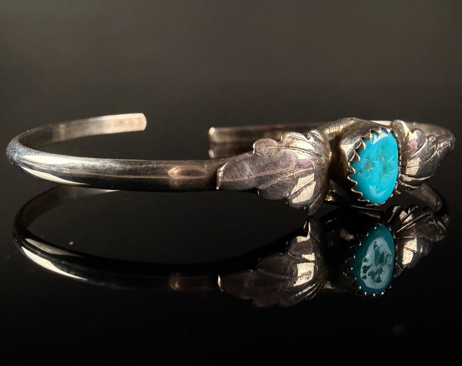Navajo Style Sterling Silver and Turquoise Leaf Motif Cuff Bracelet: A sterling silver cuff bracelet designed in the Southwestern Navajo style. The bracelet features a central oval turquoise cabochon of a bright sky blue color with minimal visible matrix. The gemstone
