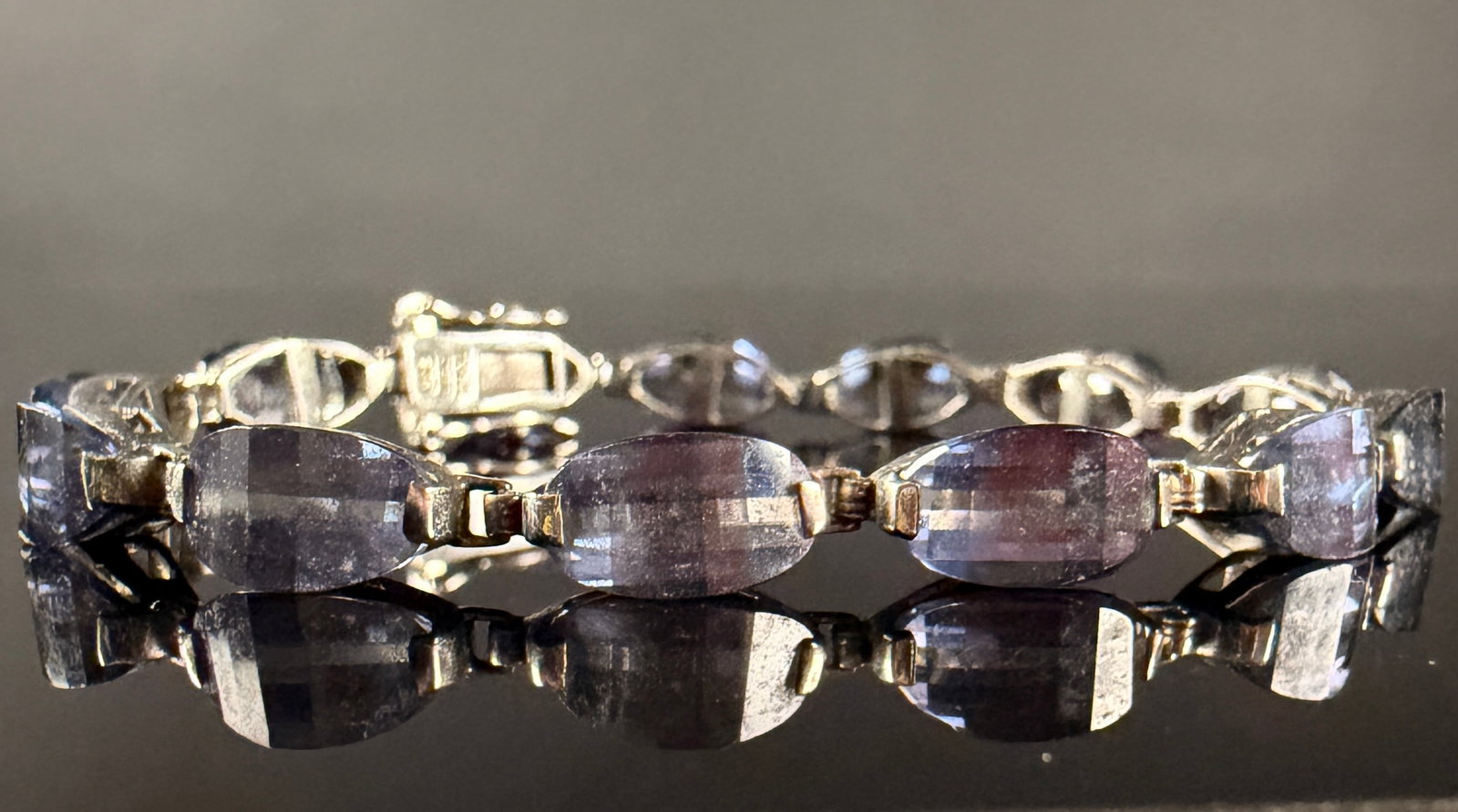 Thai Sterling Silver and Light Purple Gemstone Link Bracelet: This contemporary link bracelet is constructed of sterling silver and features thirteen faceted oval-cut gemstones of a translucent light purple hue, possibly iolite or light amethyst. The bracelet is