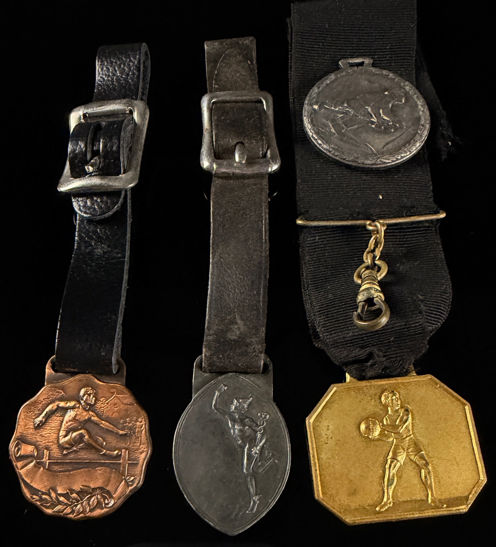 A Collection of 1915 Rochester New York Athletic Award Medals and Watch Fobs: This collection consists of vintage athletic award medals and watch fobs dating to 1915, with several pieces originating from Rochester, New York. The assortment includes track and field awards and a