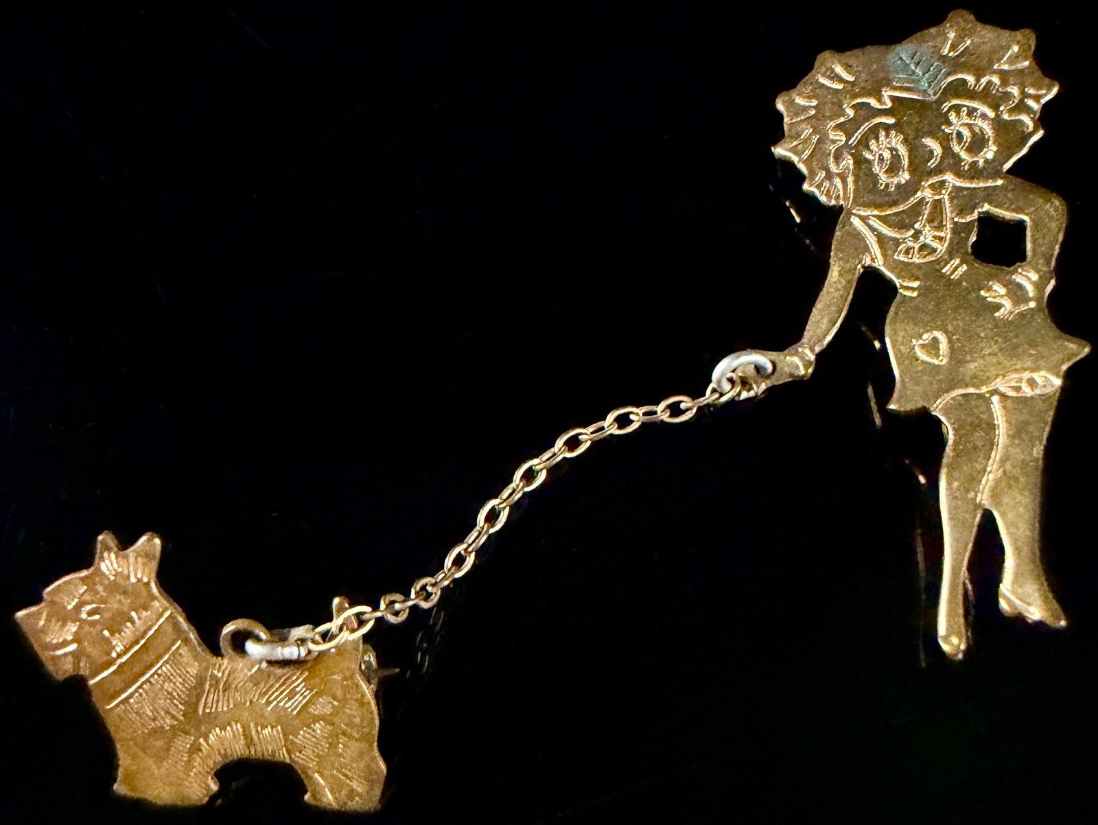 Vintage Gold-Tone Novelty Character and Scottie Dog Double Brooch Sweater Clip: This vintage double brooch or sweater clip consists of two die-stamped gold-toned base metal silhouettes connected by a fine-link chain. The larger component features a female figure in the style of t