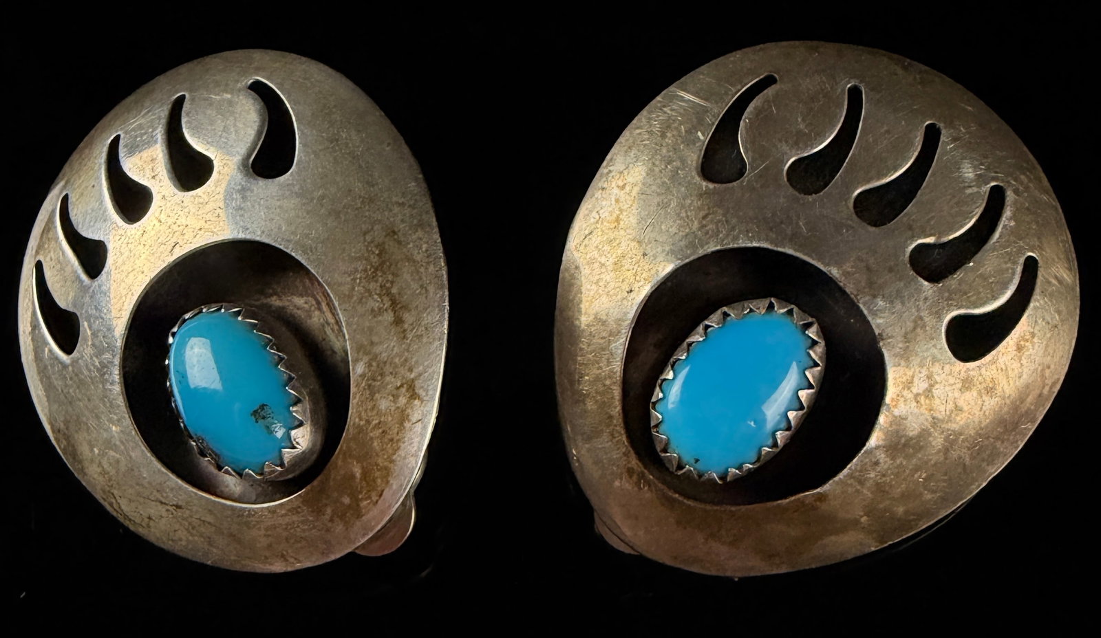 A Pair of Navajo Style Turquoise and Sterling Silver Bear Paw Shadow Box Clip-on Earrings: A matched pair of clip-on earrings in the Navajo shadow box style featuring a bear paw motif. The earrings are crafted from silver-tone metal and each contains an oval turquoise cabochon. The stones a