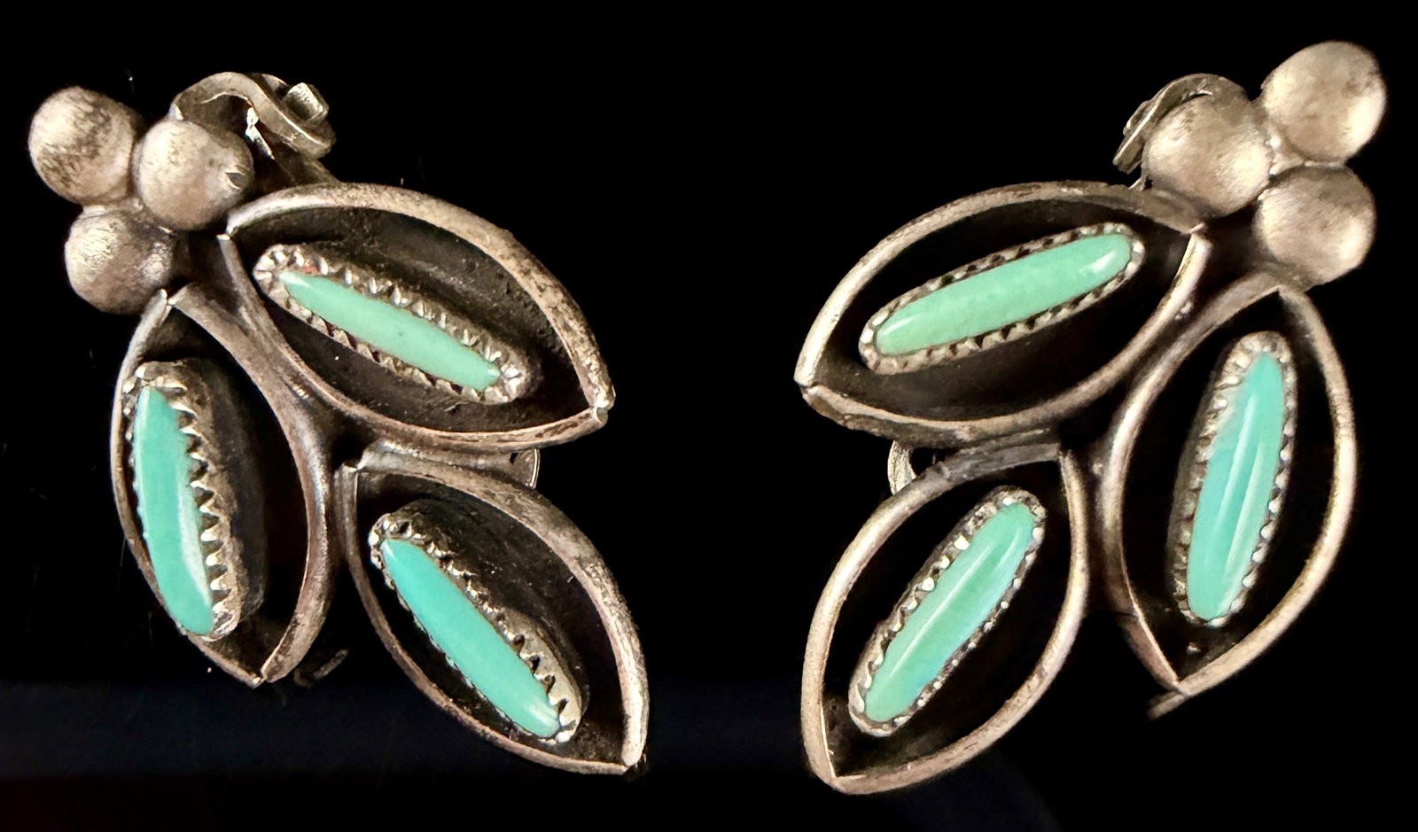 A Pair of Southwestern Style Silver Tone and Turquoise Leaf Motif Clip-On Earrings: This matched pair of Southwestern style clip-on earrings is crafted from silver-tone metal. Each earring features a botanical design composed of three leaf-shaped segments. Each segment is set with a
