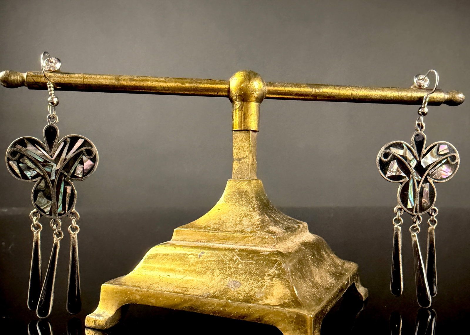 A Pair of Vintage Mexican Alpaca Silver and Abalone Inlay Dangle Earrings: This is a matched pair of Mexican dangle earrings crafted from alpaca silver, which is a non-precious nickel-copper-zinc alloy. Each earring features a central stylized trefoil motif with an openwork