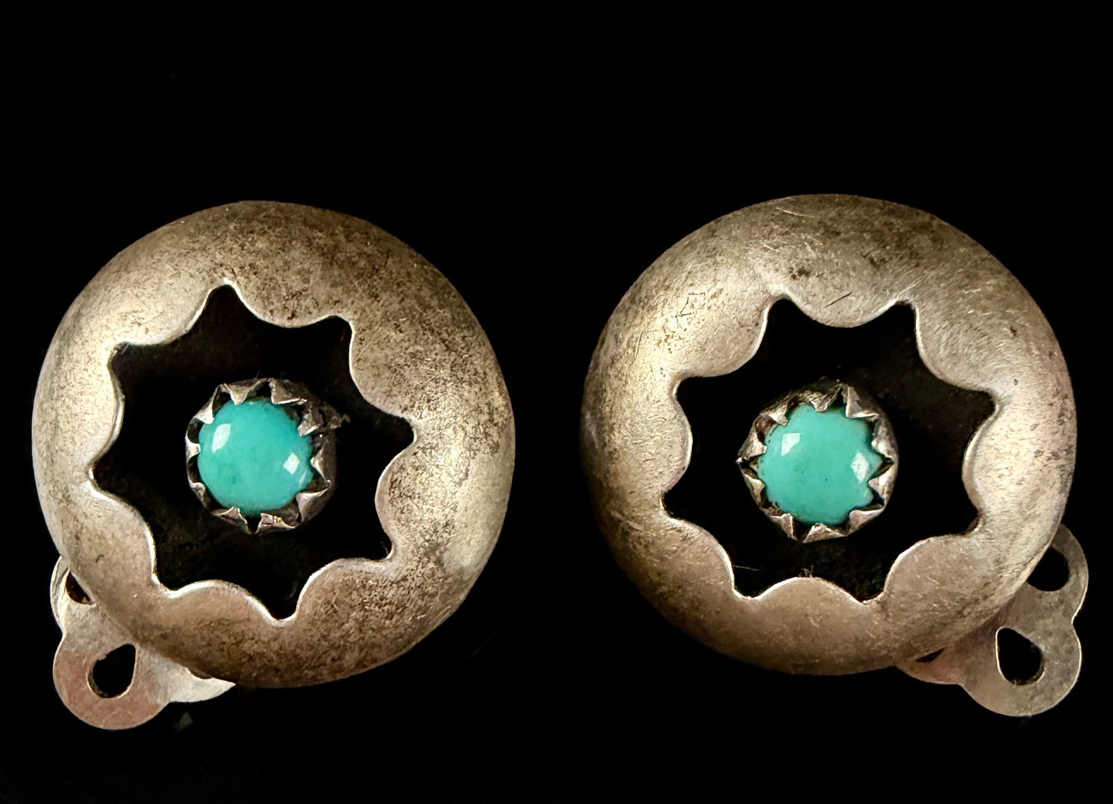 A Pair of Navajo Silver and Turquoise Concho Clip-On Earrings by Henry Preddie: A matched pair of Navajo concho earrings by jeweler Henry Preddie. Each earring is constructed as a domed circular silver concho featuring a central star-shaped scalloped cutout. At the center of each