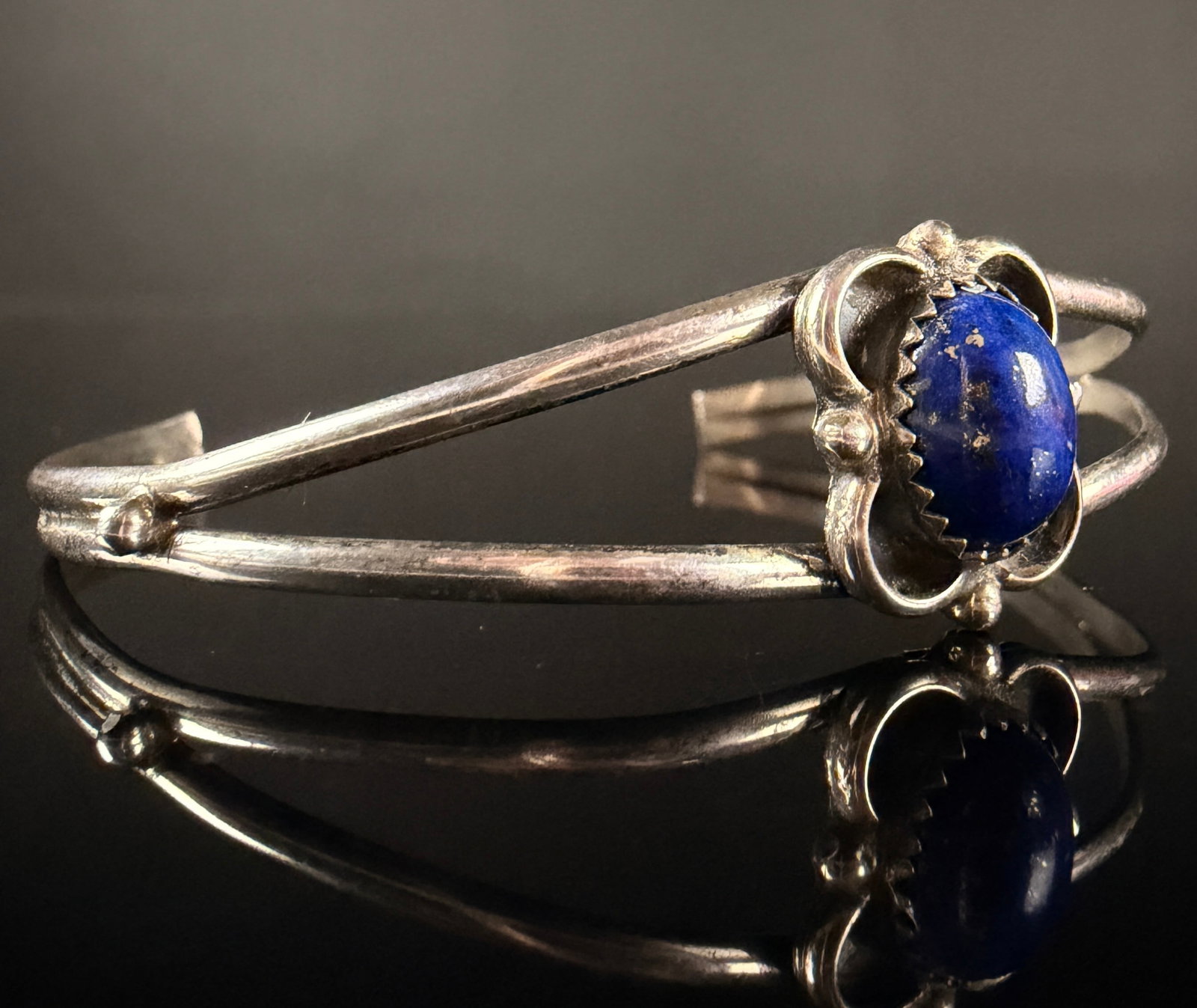 Navajo Style Silver and Lapis Lazuli Split Shank Cuff Bracelet: This Southwestern style cuff bracelet is designed with a split-shank band in silver-tone metal. The centerpiece features a single oval cabochon lapis lazuli stone with visible pyrite inclusions, secur