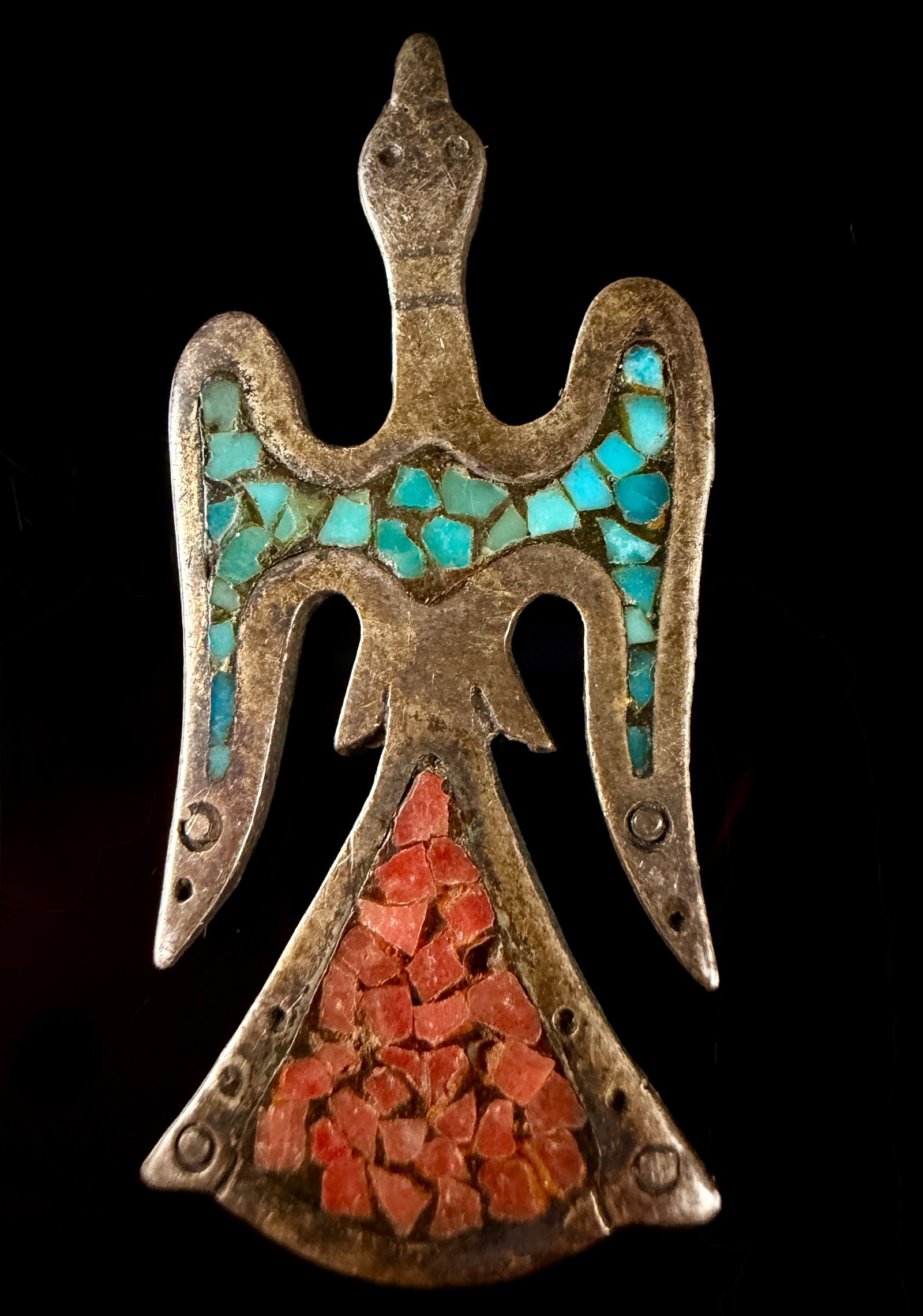 Southwest Native American Silver Thunderbird Pendant with Turquoise and Coral Chip Inlay: This stylized bird-form jewelry piece is designed in the motif of a Thunderbird or Waterbird, characteristic of Southwest Native American jewelry. The piece is constructed from silver-toned metal and