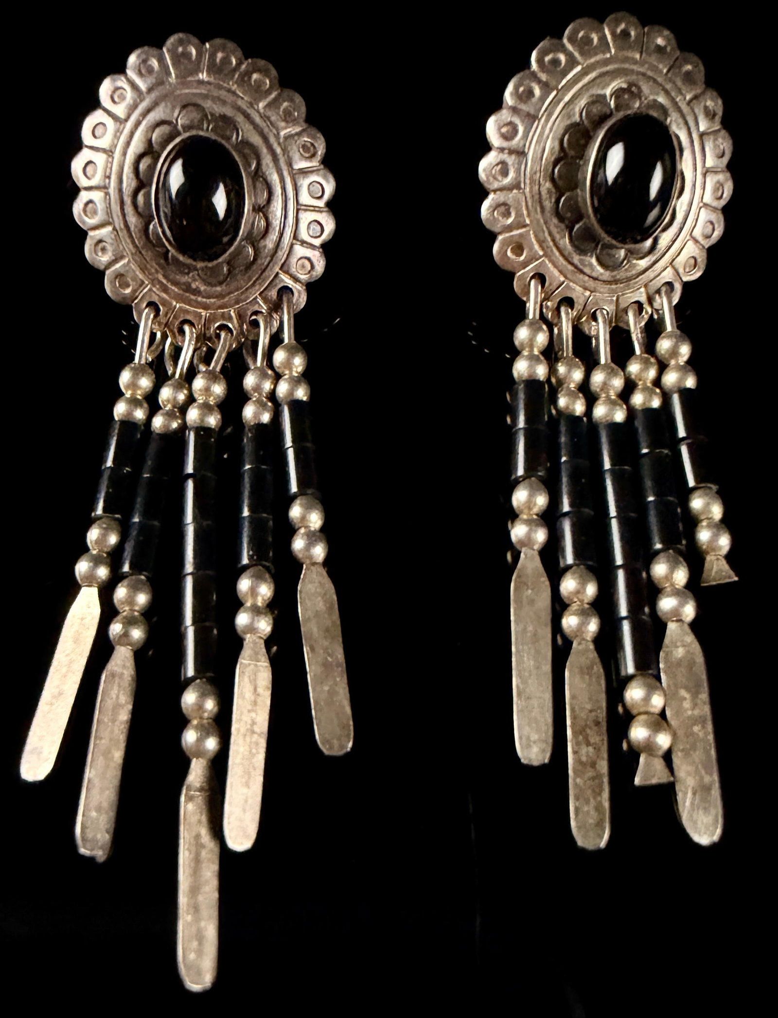 Sterling Silver and Onyx Concho Fringe Earrings: Each earring is constructed with a sterling silver concho-style top featuring a scalloped edge and stamped decorative patterns. A central oval black onyx like cabochon is bezel-set within the concho.