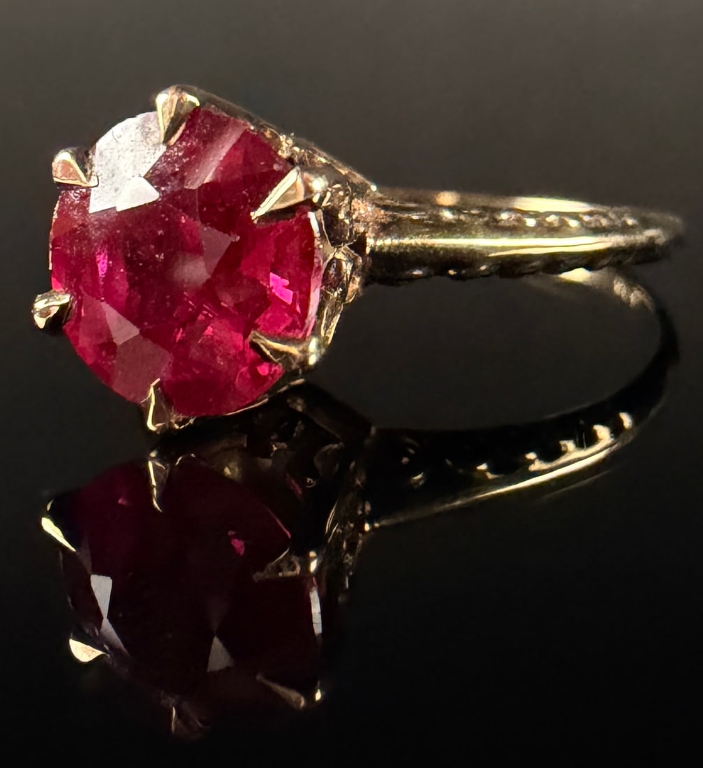 Vintage 10 Karat Yellow Gold Ruby Solitaire Ring: A vintage solitaire cocktail ring featuring a round-faceted red ruby. The gemstone is held in a high-profile six-prong setting with an openwork gallery. The 10 karat yellow gold band is decorated with