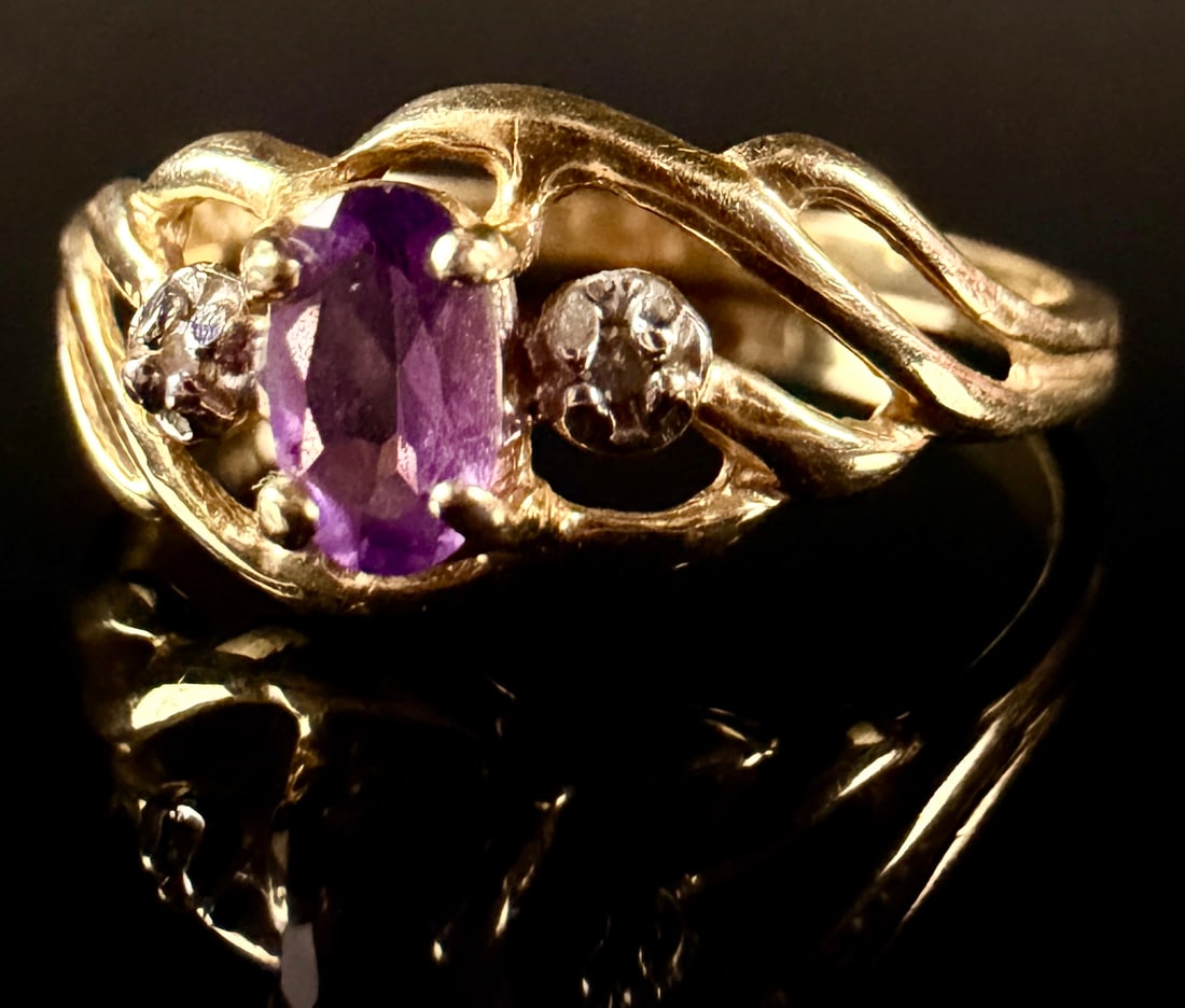 14 Karat Yellow Gold Amethyst and Diamond Bypass Ring: A 14 karat yellow gold fashion ring featuring a three-stone bypass design. The center setting contains one prong-set oval-cut purple amethyst measuring approximately 6mm by 4mm. Flanking the center st
