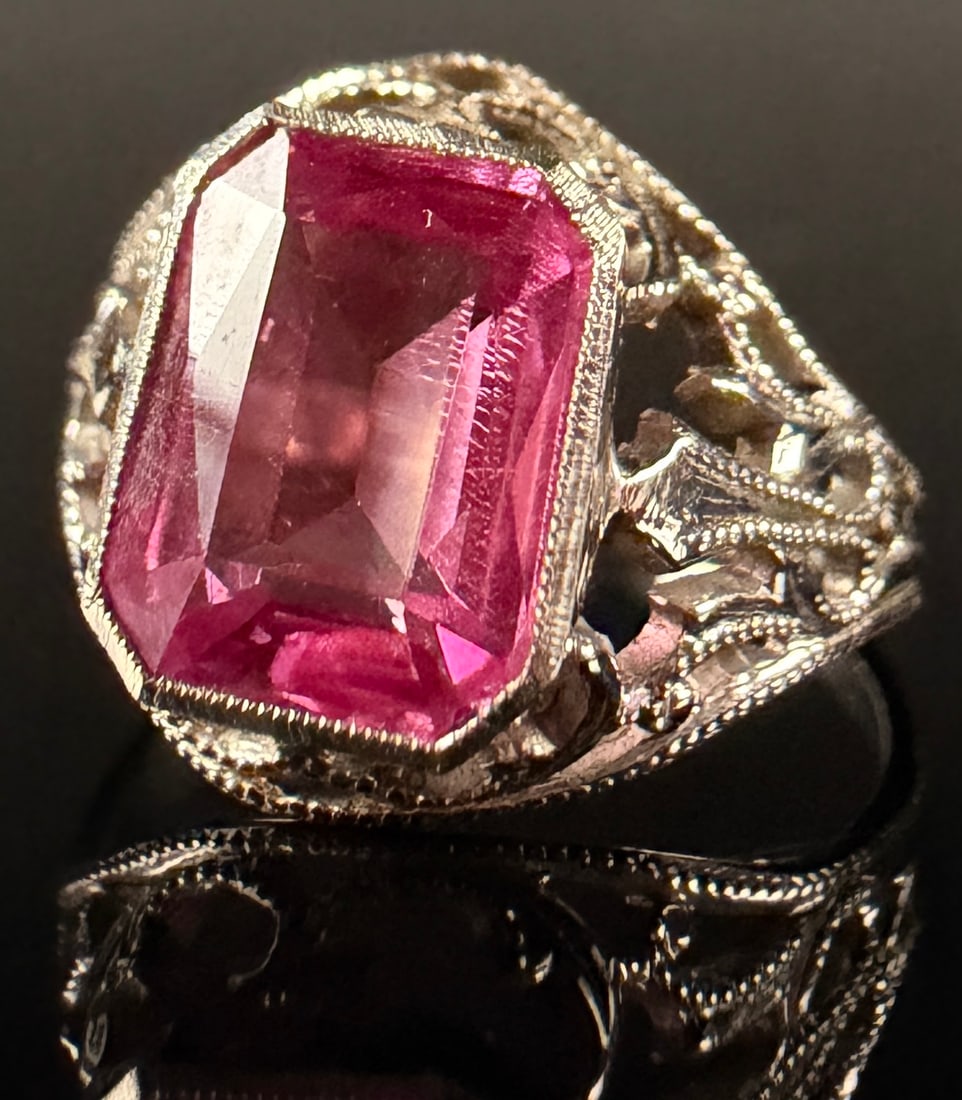 Art Deco Style 14 Karat White Gold and Pink Sapphire Filigree Ring: This Art Deco style cocktail ring is constructed of 14 karat white gold, as confirmed by electronic gold testing. The center of the ring features one emerald-cut pink stone secured in a rectangular be