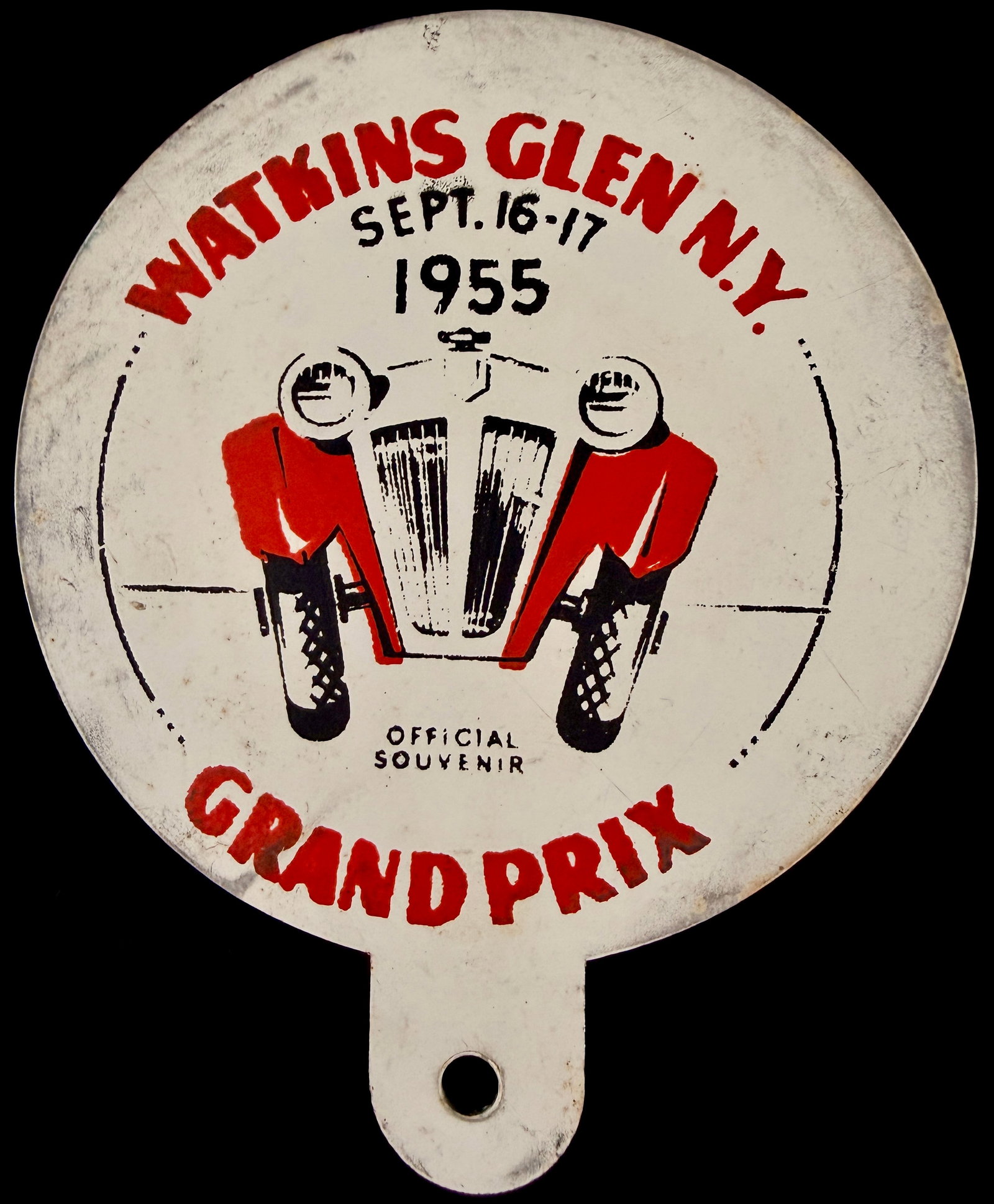 1955 Watkins Glen Grand Prix Official Souvenir License Plate Topper: This is an official souvenir license plate topper commemorating the Watkins Glen Grand Prix held on September 16-17, 1955. The item is constructed of circular metal with a white-coated finish. The obv