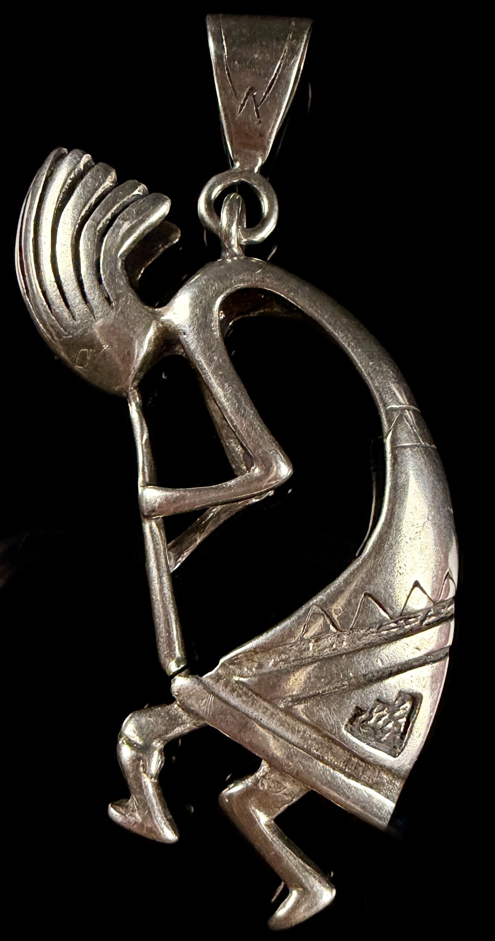 Bennett Sterling Silver Kokopelli Pendant: This large sterling silver pendant by Bennett depicts the Southwestern deity Kokopelli, a humpbacked flute player, in a stylized and dynamic dancing pose. The piece is crafted with a high-polish finis