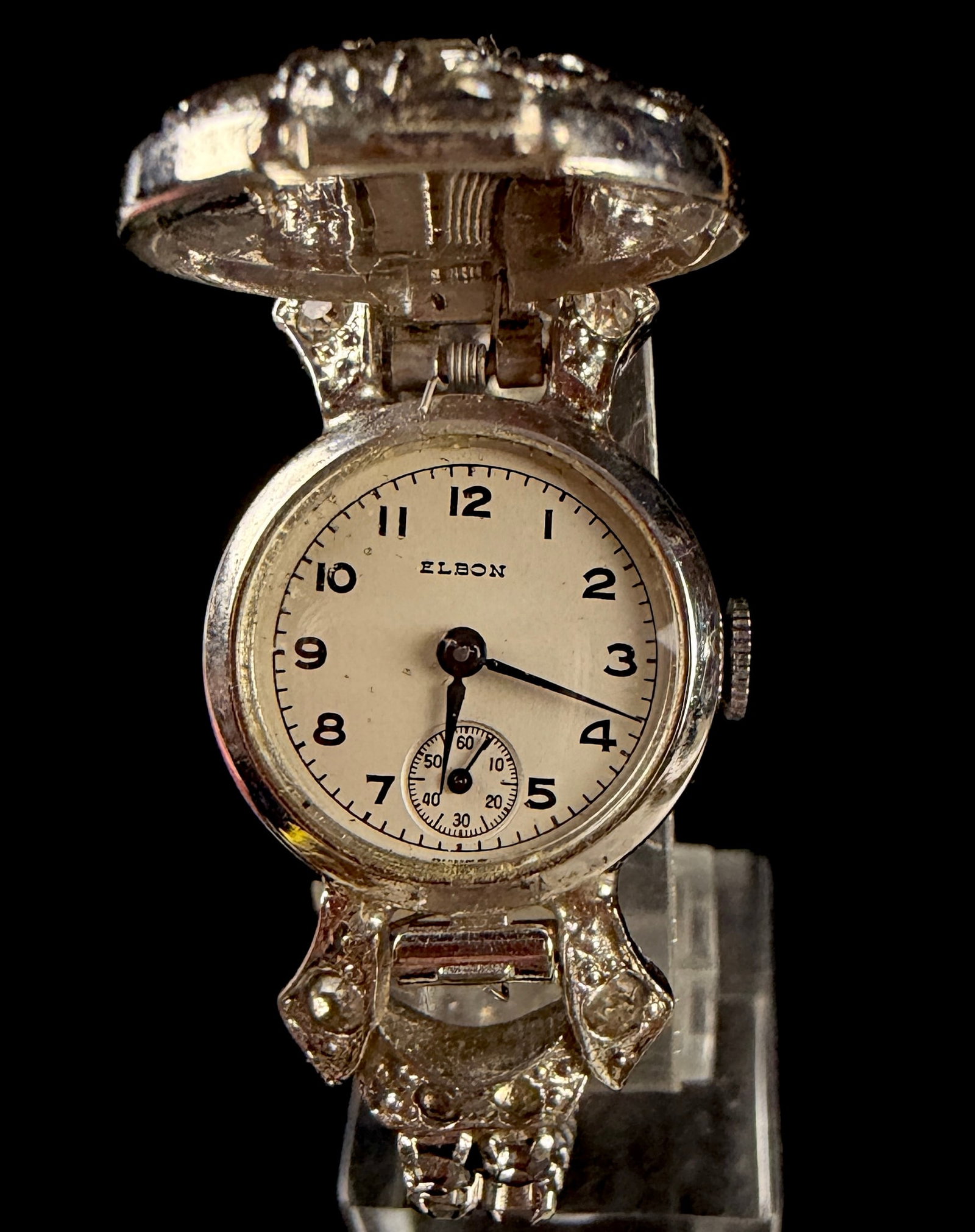 Vintage Elbon Swiss Manual Wind Secret Bracelet Watch: This vintage Elbon Swiss manual wind wristwatch is designed as a secret bracelet watch. The silver-tone case features a hinged, dome-shaped cover set with various colorless stones in a swirling motif,