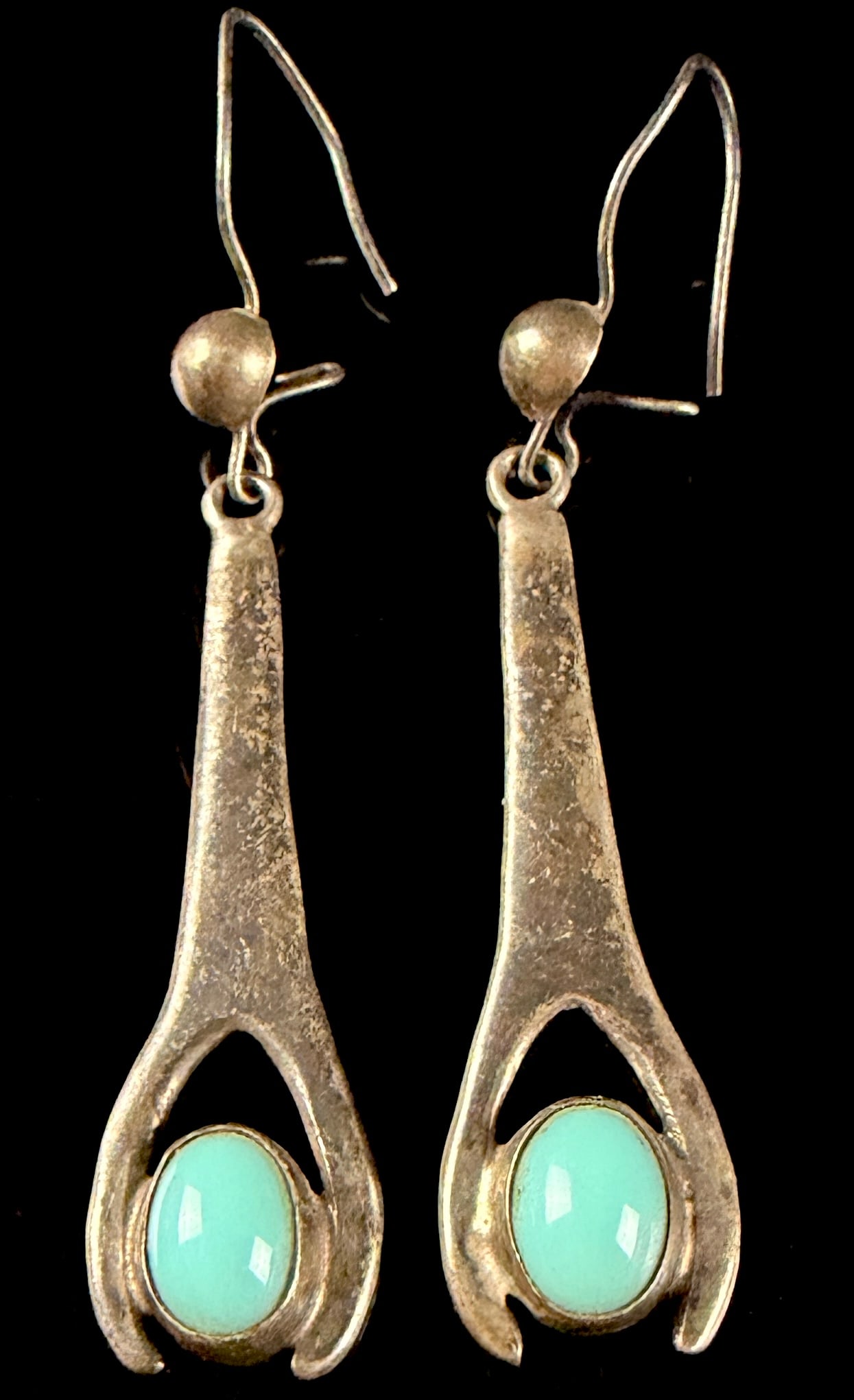 A Pair of Mexican Sterling Silver and Cabochon Drop Earrings marked PCM: A pair of sterling silver drop earrings featuring a tapered, openwork frame. Each earring is set with a bezel-set oval cabochon of a light blue-green color resembling turquoise or chrysocolla. The ear