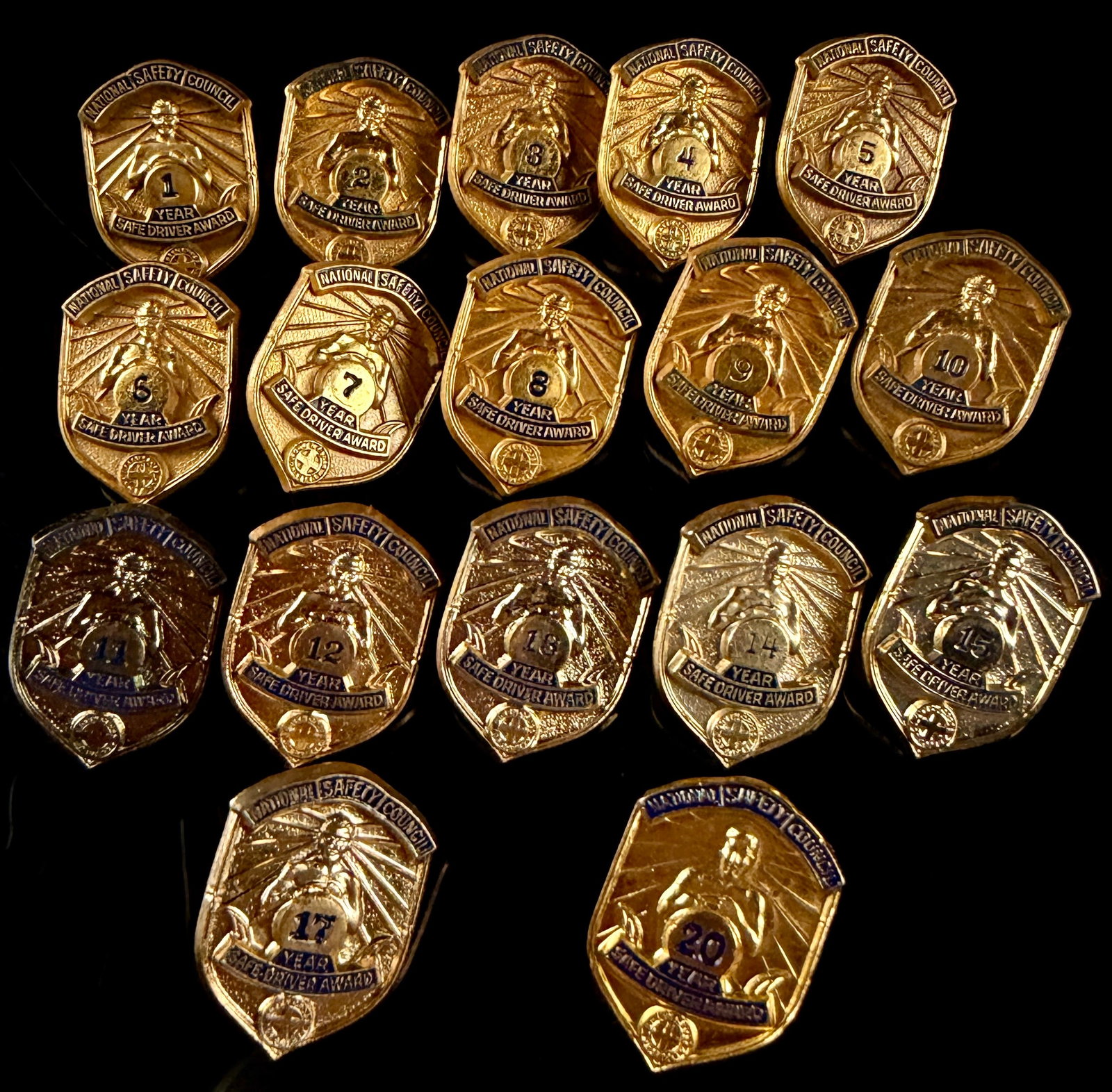 Collection of 17 Vintage US National Safety Council Safe Driver Award Lapel Pins: This lot consists of 17 vintage lapel pins issued by the National Safety Council of the United States to recognize milestones in safe driving. Each shield-shaped pin features a central embossed figure