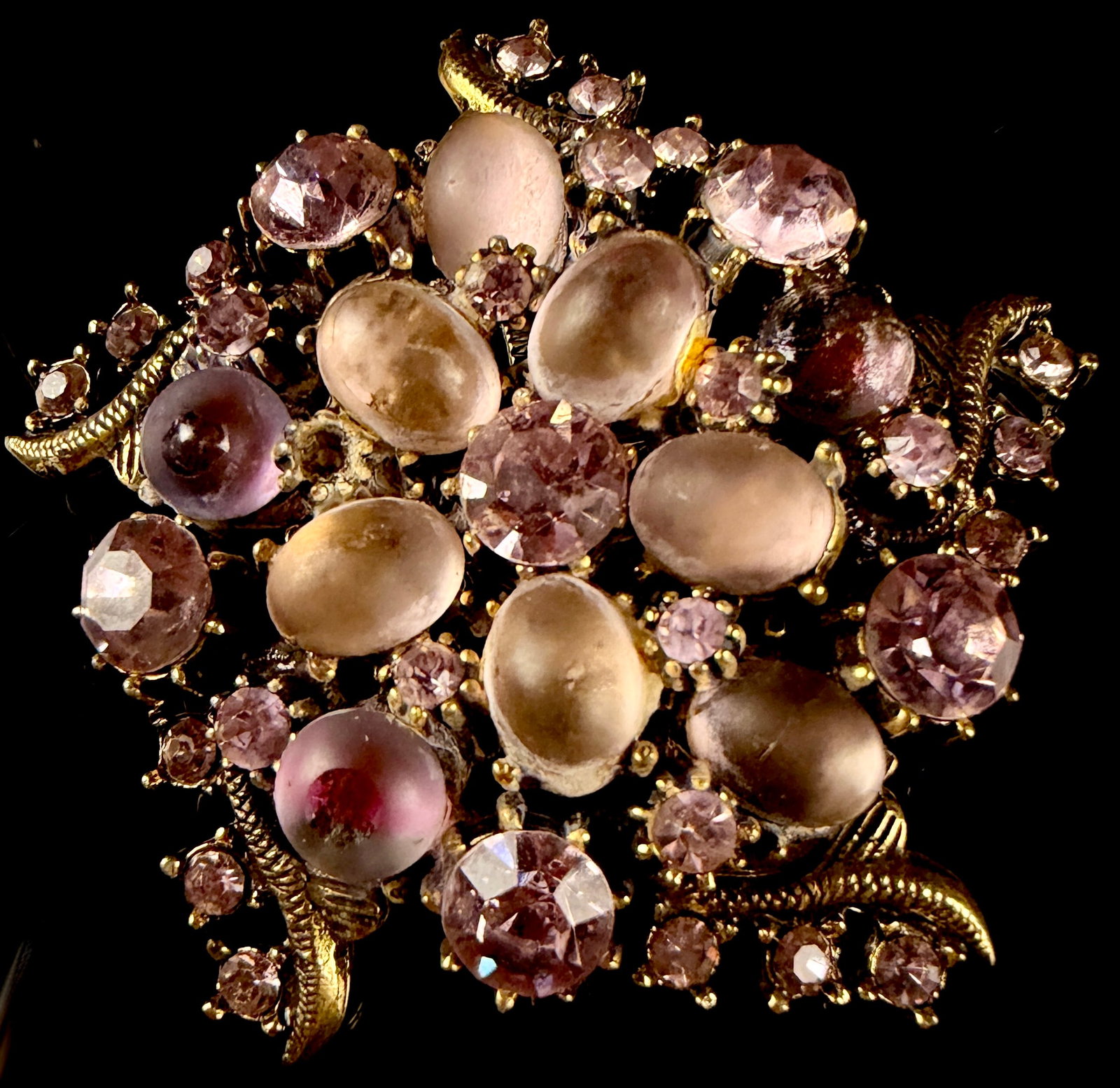 Florenza Vintage Pink and Lilac Glass Rhinestone and Cabochon Floral Spray Brooch: This vintage costume jewelry brooch is by the American maker Florenza. The design is a multidimensional floral and foliate spray, featuring textured gold-tone metal elements with a scaly pattern integ