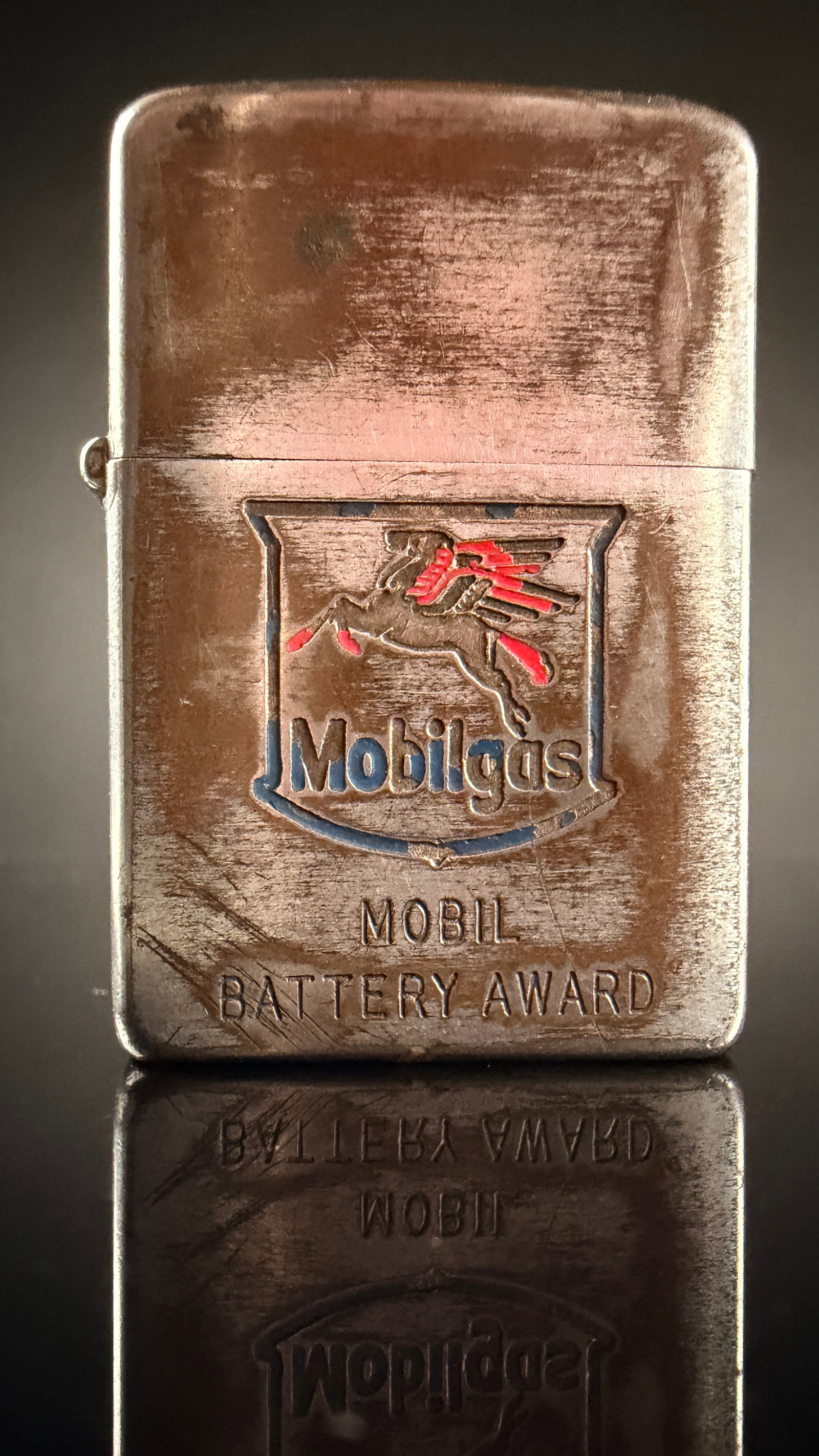 Vintage Zippo Mobilgas Battery Award Pocket Lighter: A vintage windproof pocket lighter manufactured by the Zippo Manufacturing Company in Bradford, Pennsylvania. The item features a five-barrel hinge and a flat bottom case design. The front face is dec
