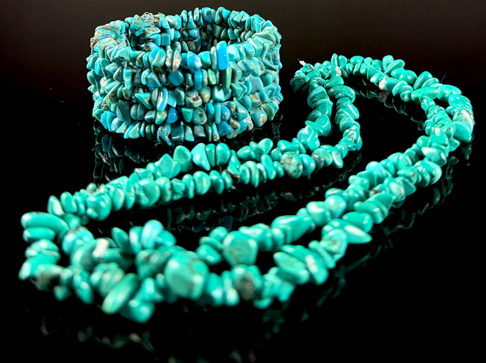 Two Turquoise-Colored Stone Chip Jewelry Items: A Necklace and Multi-Row Coil Bracelet: This jewelry set consists of a long, continuous-strand necklace and a multi-row wrap-around bracelet. Both pieces are constructed with tumbled, irregular stone chips in varying shades of blue and gree