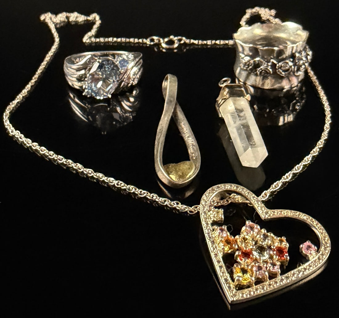 An Assortment of Sterling Silver Jewelry Including a Multi-Gemstone Heart Pendant and Designer Rings: This collection of sterling silver jewelry includes multiple items with various designs and designer hallmarks. Included is a sterling silver ring set with a large oval faceted light blue gemstone, ap