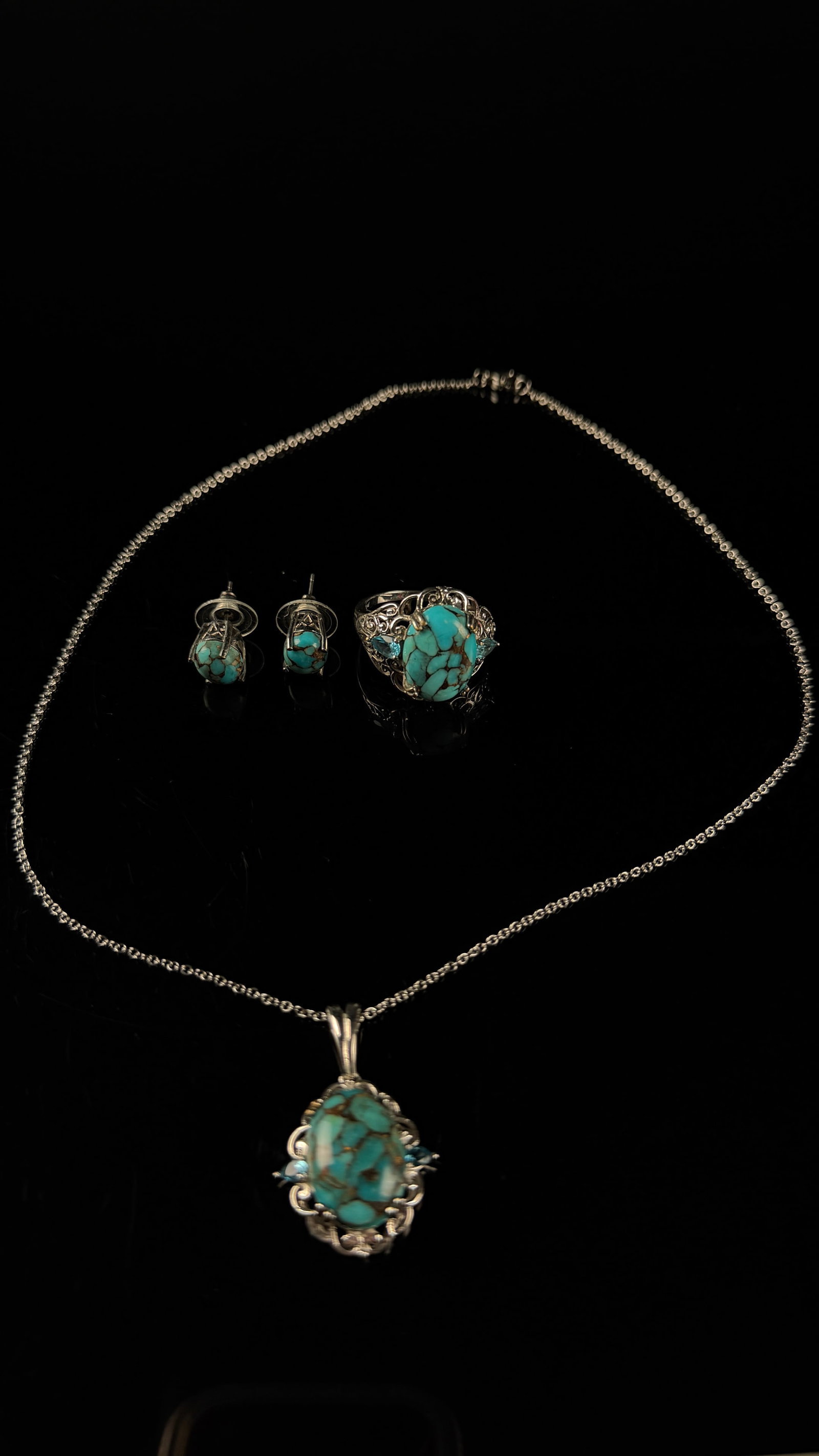 A Set of Southwestern Style Silver Toned Jewelry with Turquoise and Blue Gemstones: A set of silver-toned jewelry comprising a pendant necklace, a ring, and a pair of stud earrings. The suite features oval and round turquoise cabochons characterized by a brown spiderweb matrix. The p