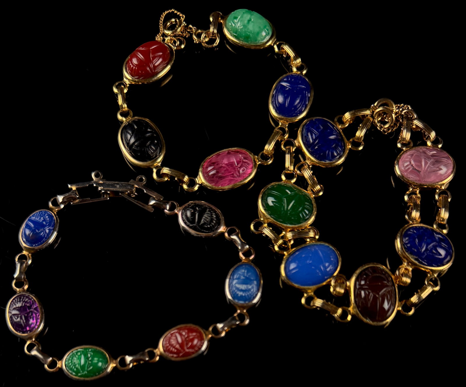 Three Vintage Egyptian Revival Multi-Stone Scarab Link Bracelets: A collection of three vintage mid-century Egyptian Revival style link bracelets featuring multi-colored carved scarab cabochons. Each bracelet is composed of oval stones traditionally carved with a be