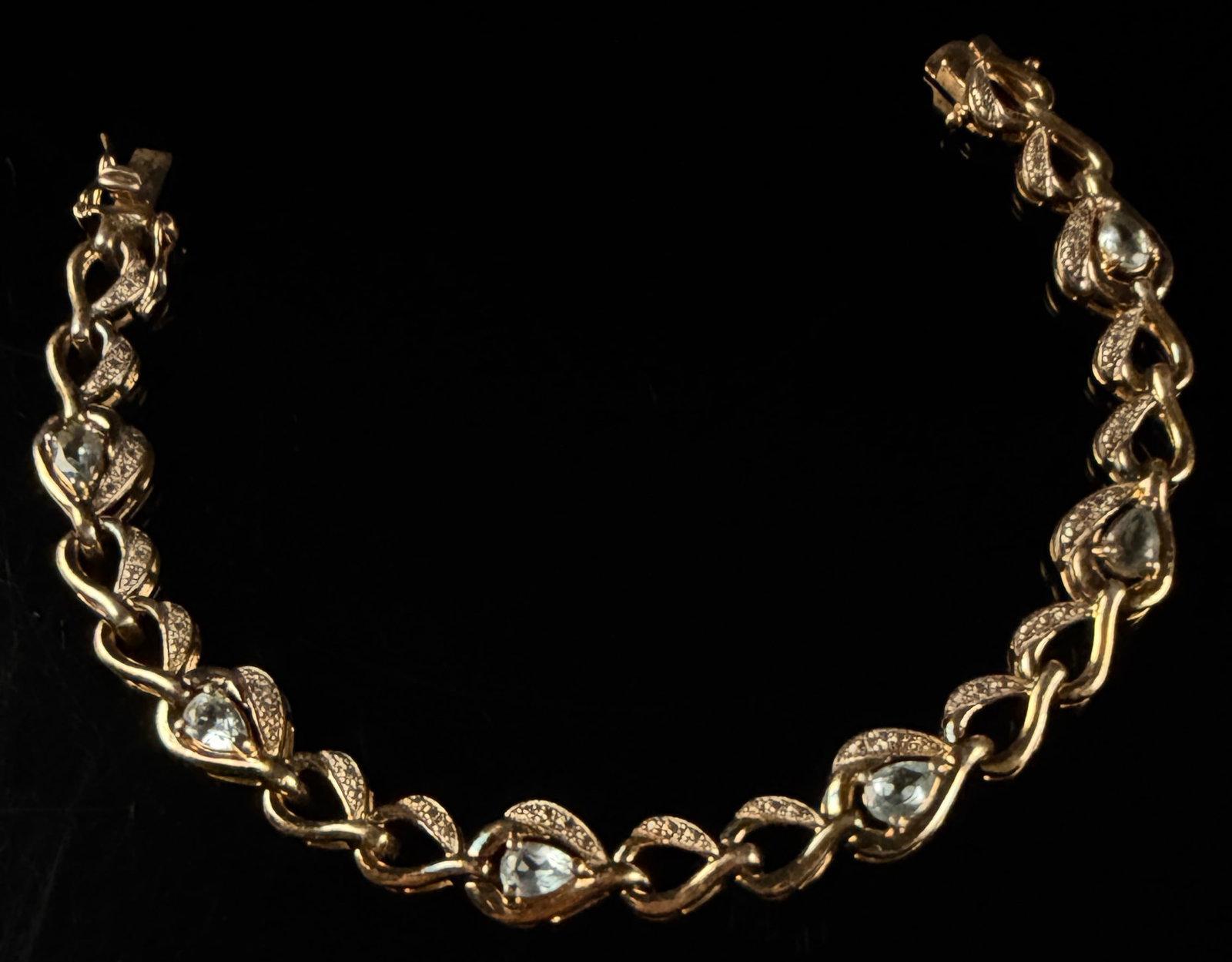 JR Gold-Plated Sterling Silver and Cubic Zirconia Link Bracelet: A yellow gold-plated sterling silver link bracelet featuring a series of interlocking wave-style links. The design incorporates five primary links set with pear-cut light blue cubic zirconia, each acc