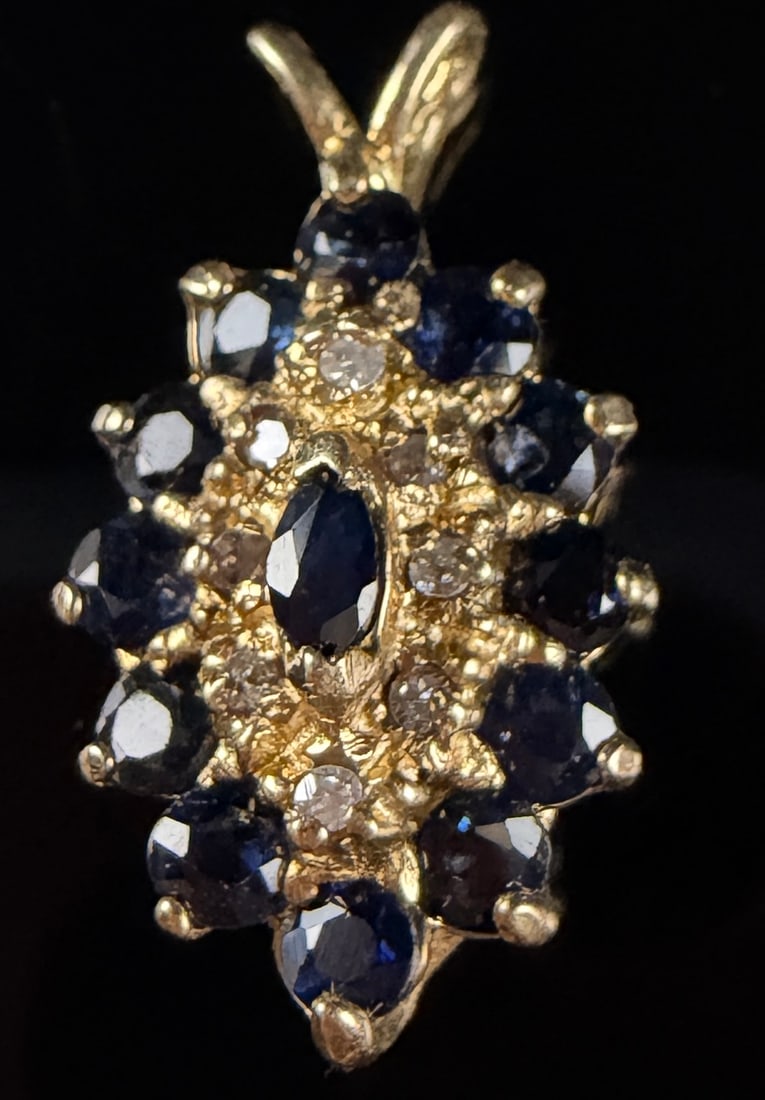 14K Yellow Gold Sapphire and Diamond Navette Cluster Pendant: A 14K yellow gold navette-shaped cluster pendant featuring a tiered gemstone arrangement. The center is set with a single marquise-cut dark blue sapphire, elevated above the surrounding stones. The mi