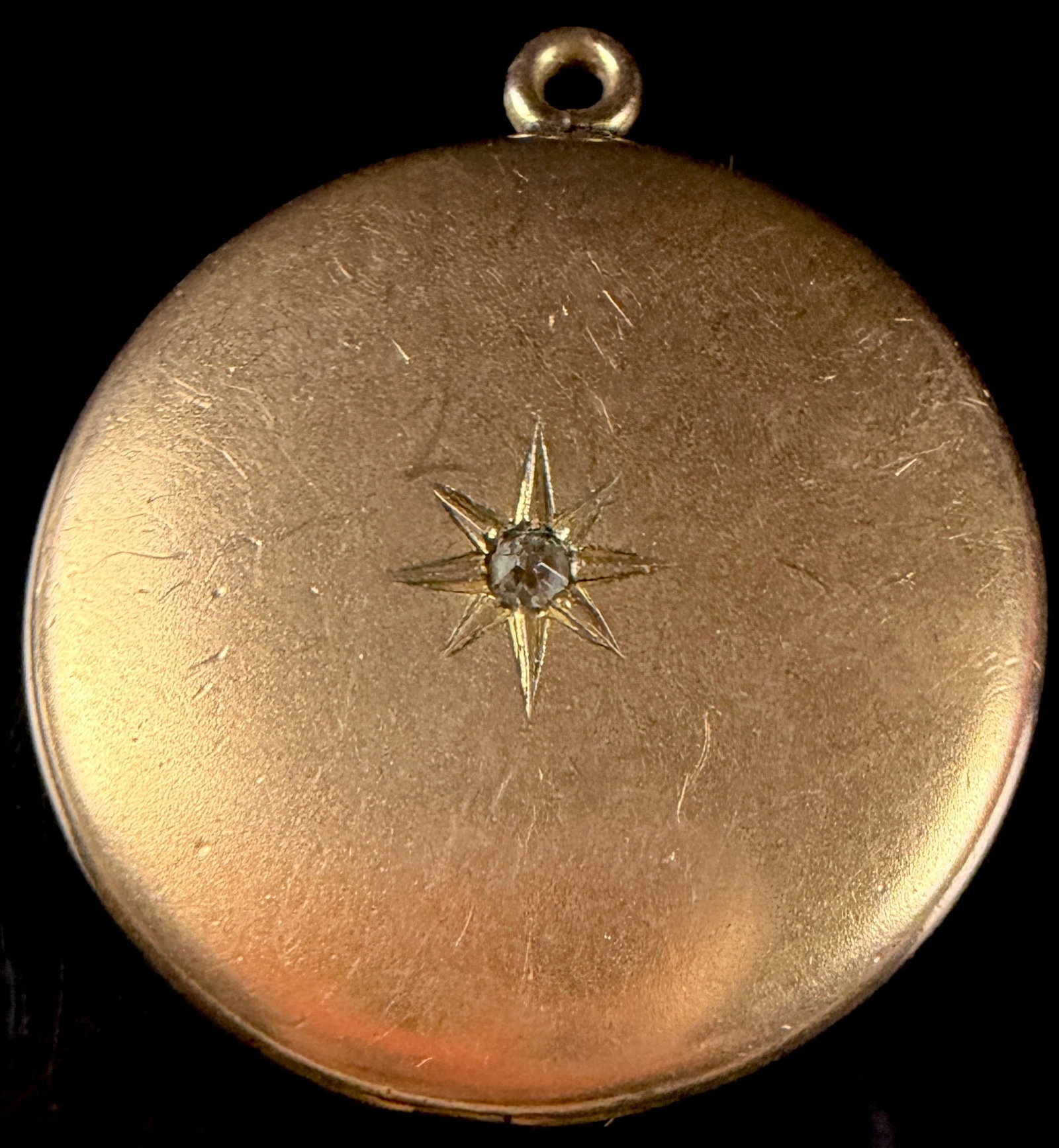 Victorian Style Yellow Gold Tone Starburst Locket with Clear Gemstone: A circular locket pendant designed in the Victorian style, featuring a yellow gold-tone finish. The front face is decorated with an engraved eight-point starburst motif, grain-set with a single small,